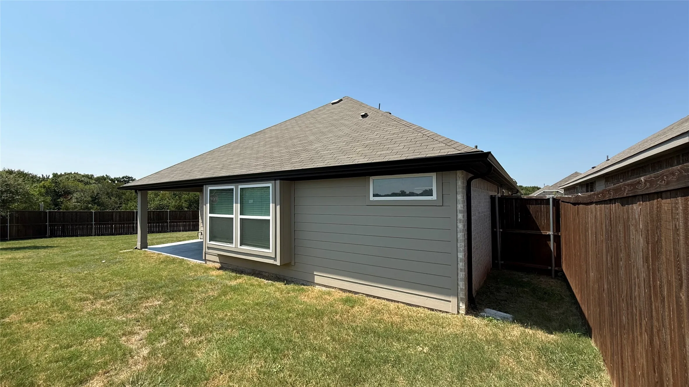 Expansive backyard featuring a covered patio, durable wood fencing, and a bay window