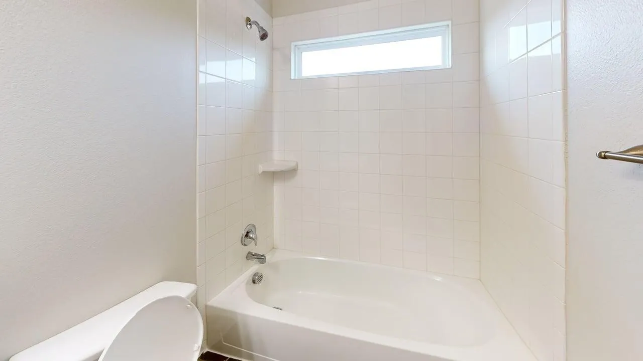 Bathroom featuring a white tiled shower surround, recessed window, built-in soap dish, and a tub/shower combination with chrome fixtures