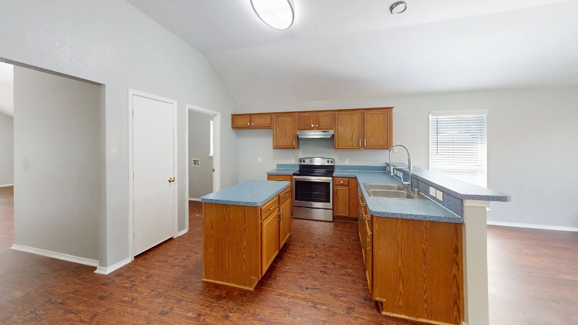 Spacious kitchen featuring wood cabinetry, a central island with countertop seating, stainless steel appliances, dual sinks, and wood-finish flooring throughout
