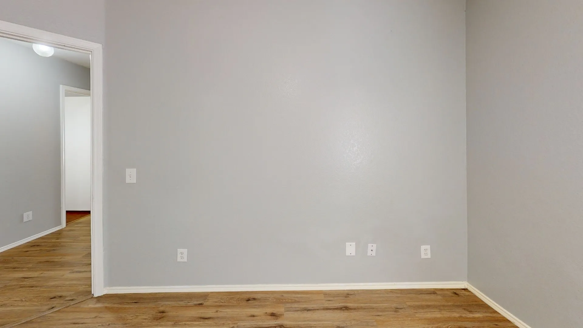 Bright, open room featuring warm wood-finish flooring, freshly painted walls, and multiple electrical outlets