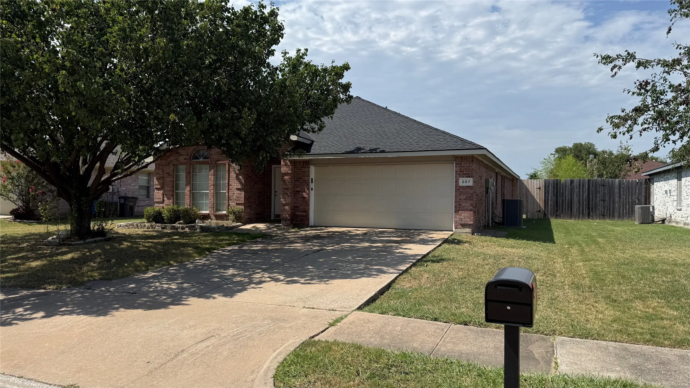 Charming brick home featuring a spacious driveway, two-car garage, and mature shade trees on the front grounds