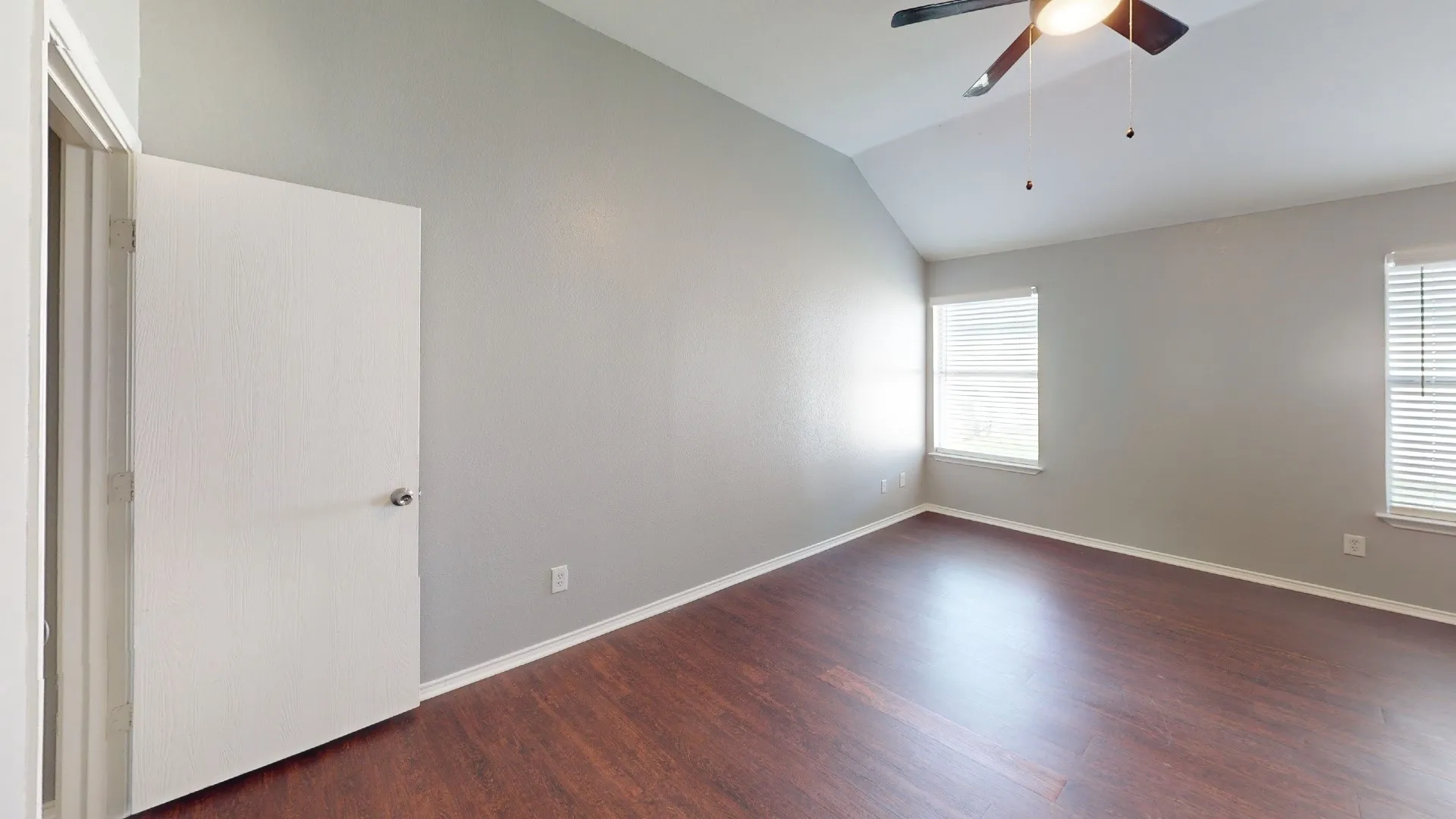 Vaulted ceiling, wood-finish flooring, two windows with blinds, ceiling fan with integrated lighting, and neutral wall tones
