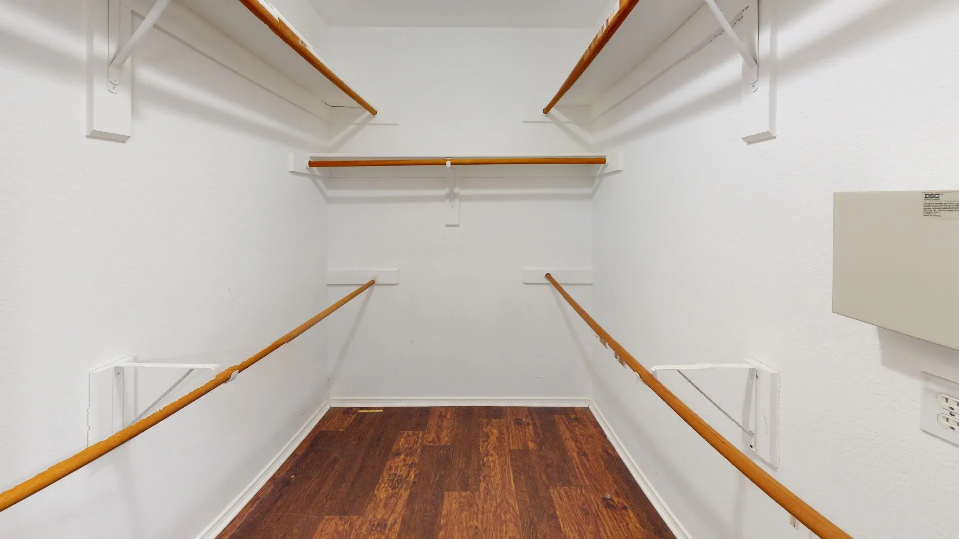 Walk-in closet with multiple white shelving units and wood-finish flooring