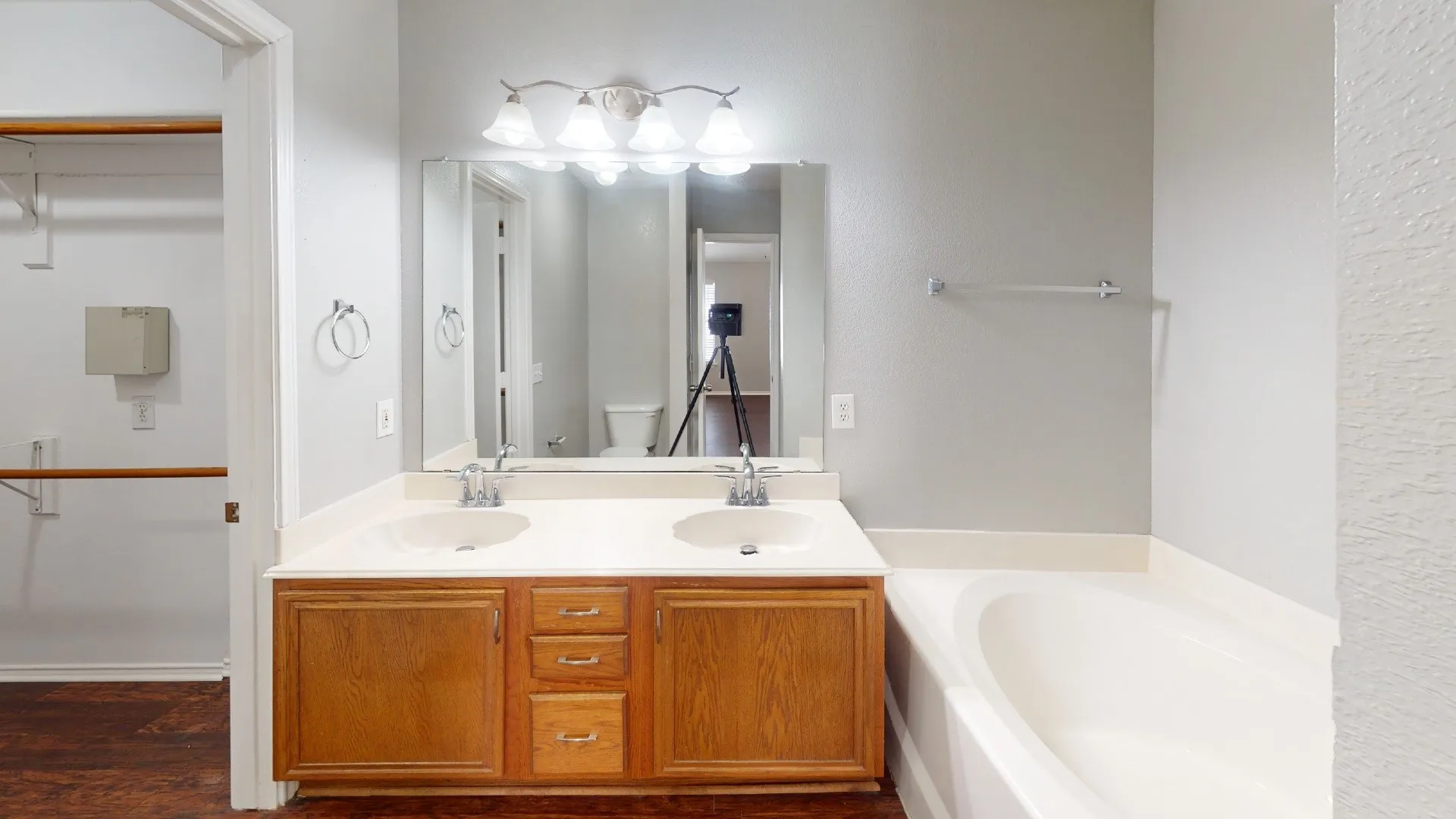 Double vanity with wood-finish cabinetry and integrated sinks, large mirror, and an adjacent built-in bathtub