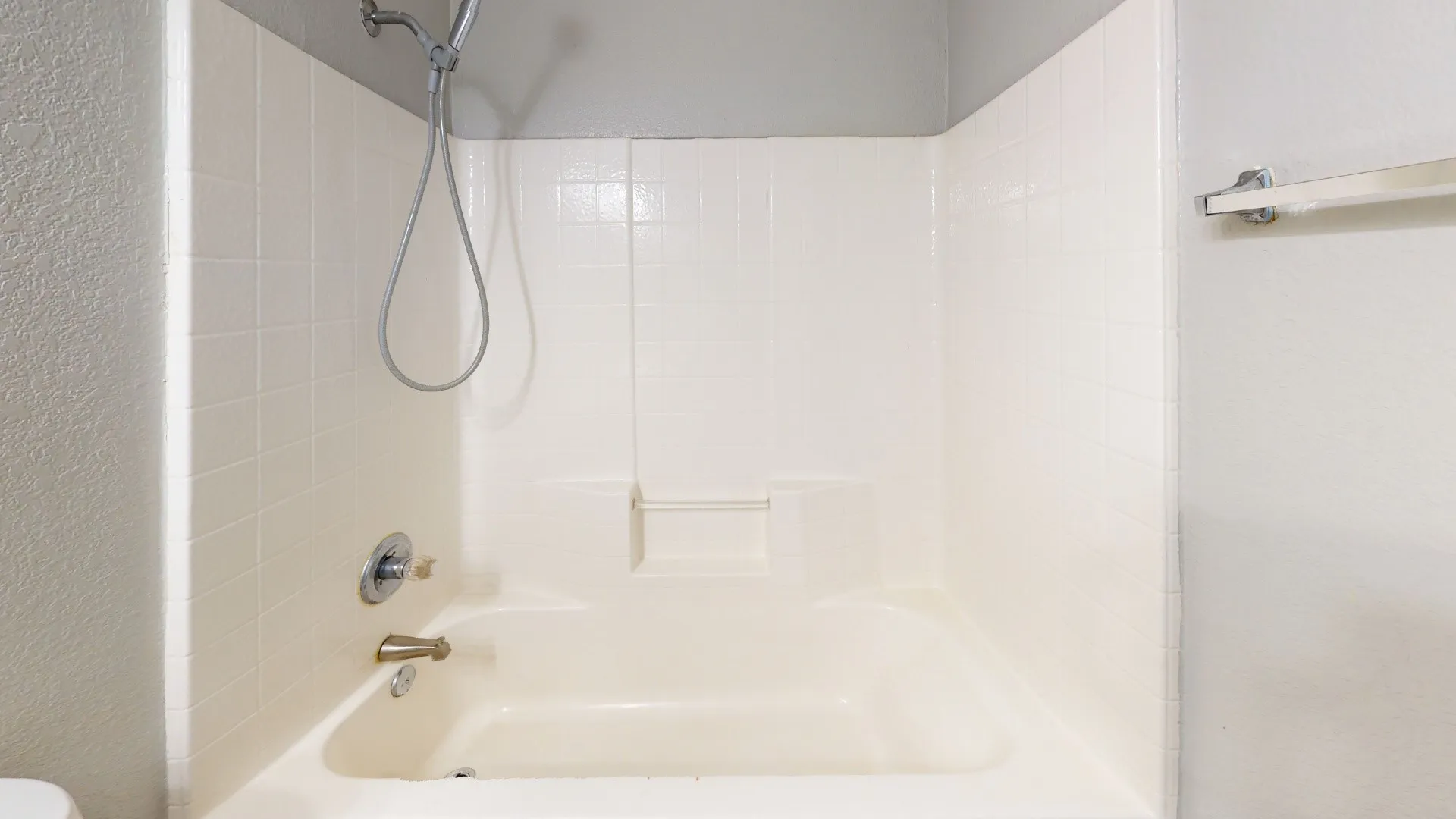 Bathtub and shower combination with a handheld showerhead, chrome fixtures, and a built-in shelf