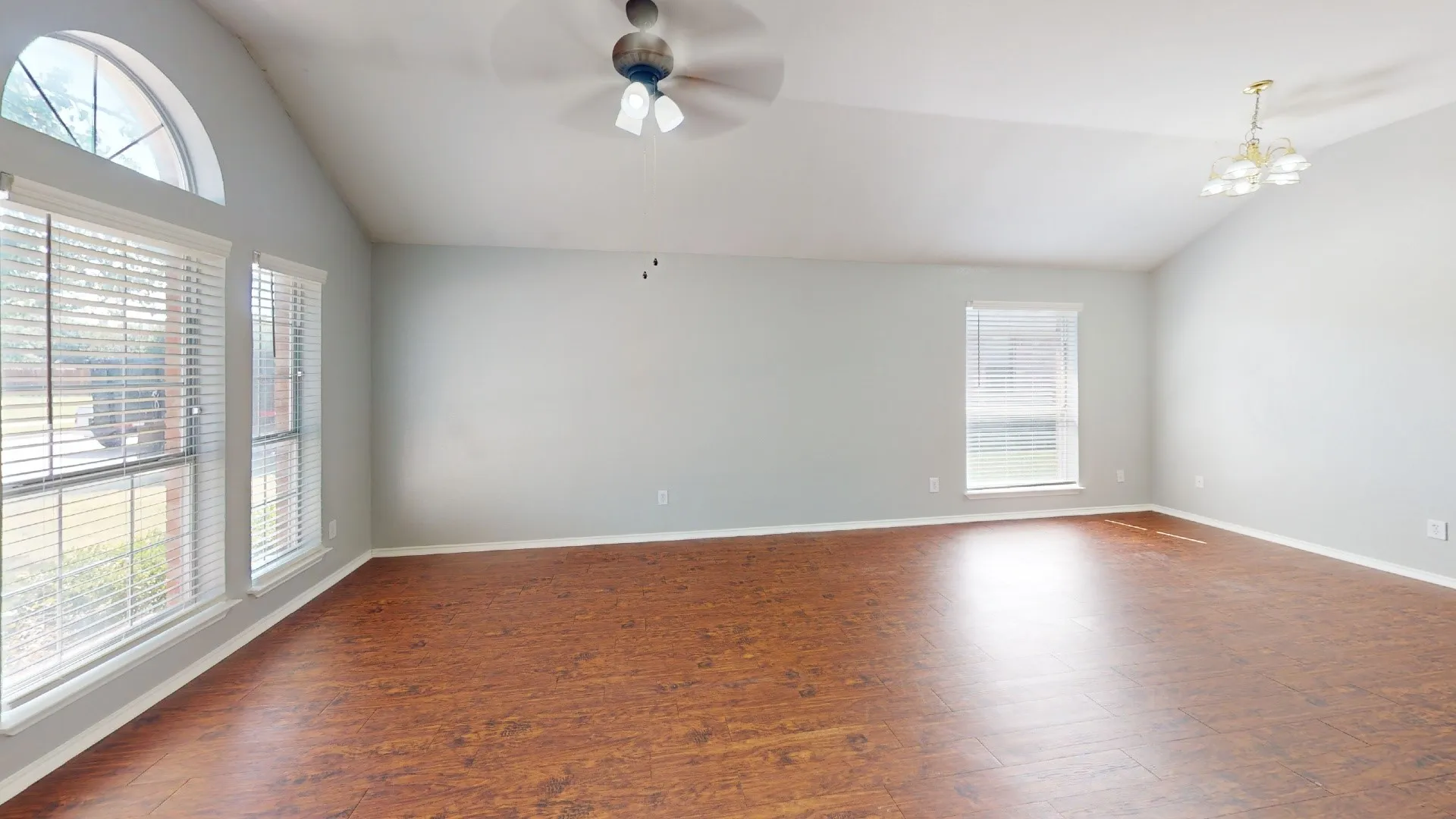 Vaulted ceiling, wood-finish flooring, arched transom window, ceiling fan, and chandelier