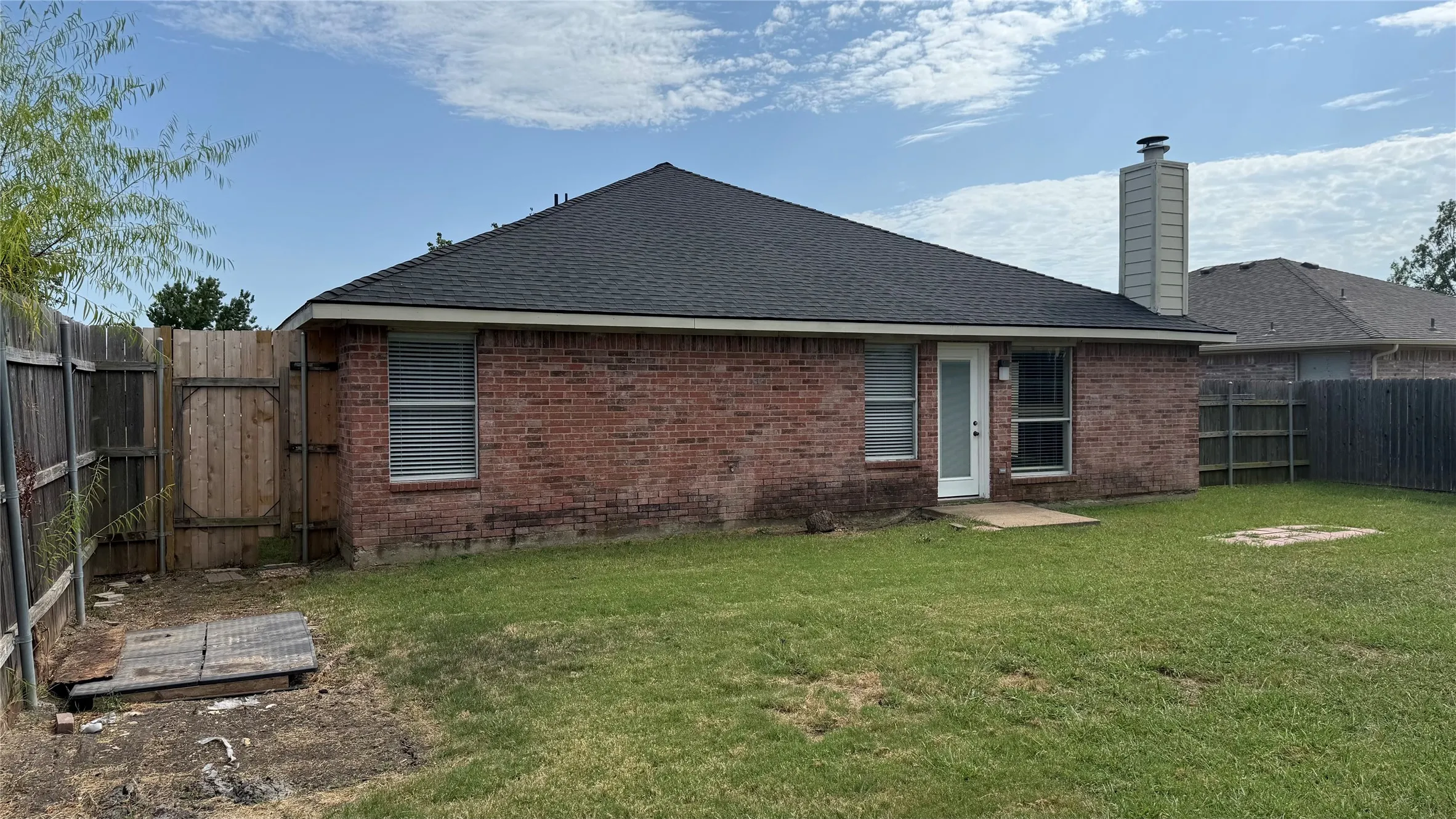 Brick exterior with a dark shingle roof, a light-colored chimney, and a white back door