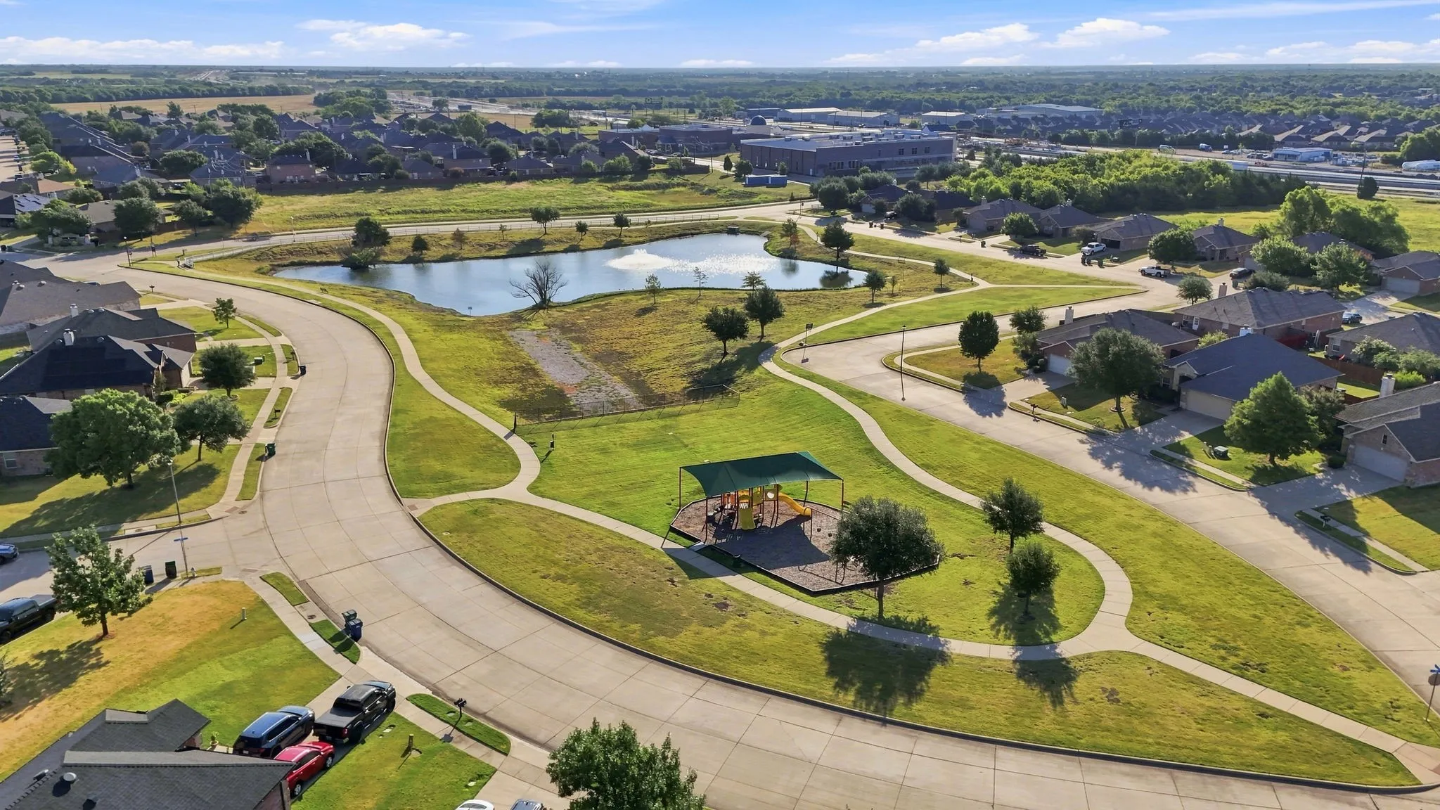 Community green space with walking paths, a pond, and a shaded playground structure, surrounded by residential properties