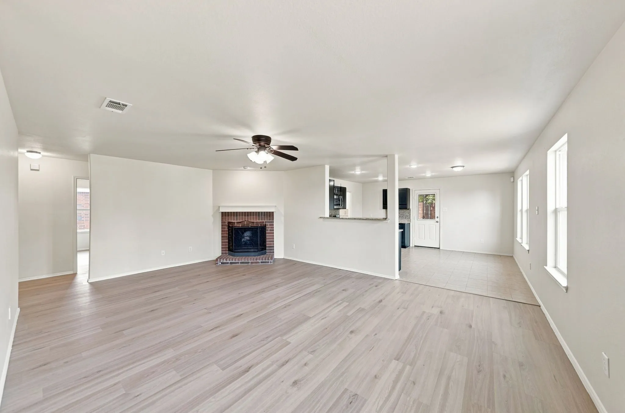 Spacious interior featuring light wood-finish flooring, a brick fireplace, a ceiling fan, and multiple windows