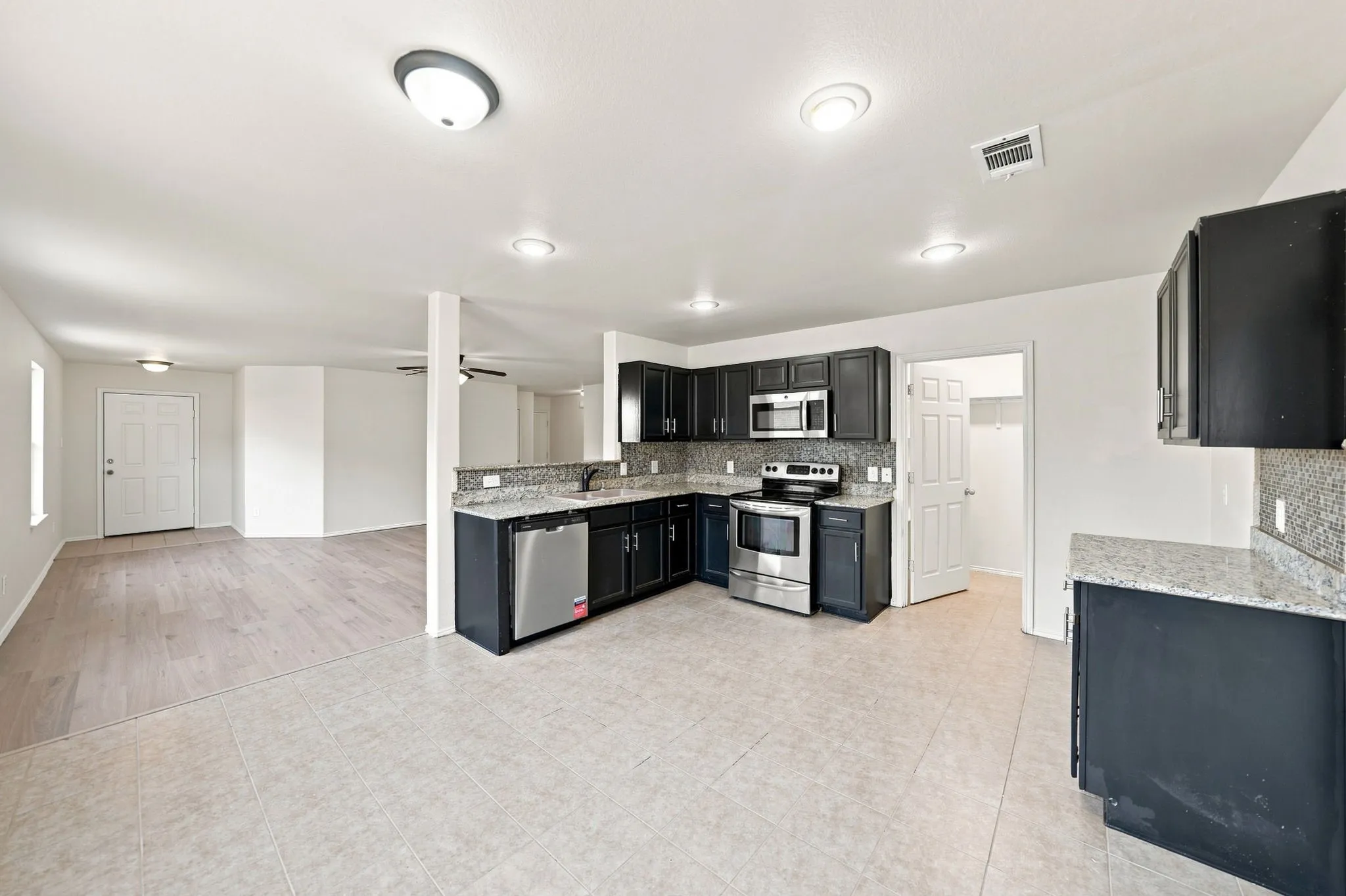 Kitchen featuring stainless steel appliances, dark wood-finish cabinetry, light-toned countertops, and a full backsplash