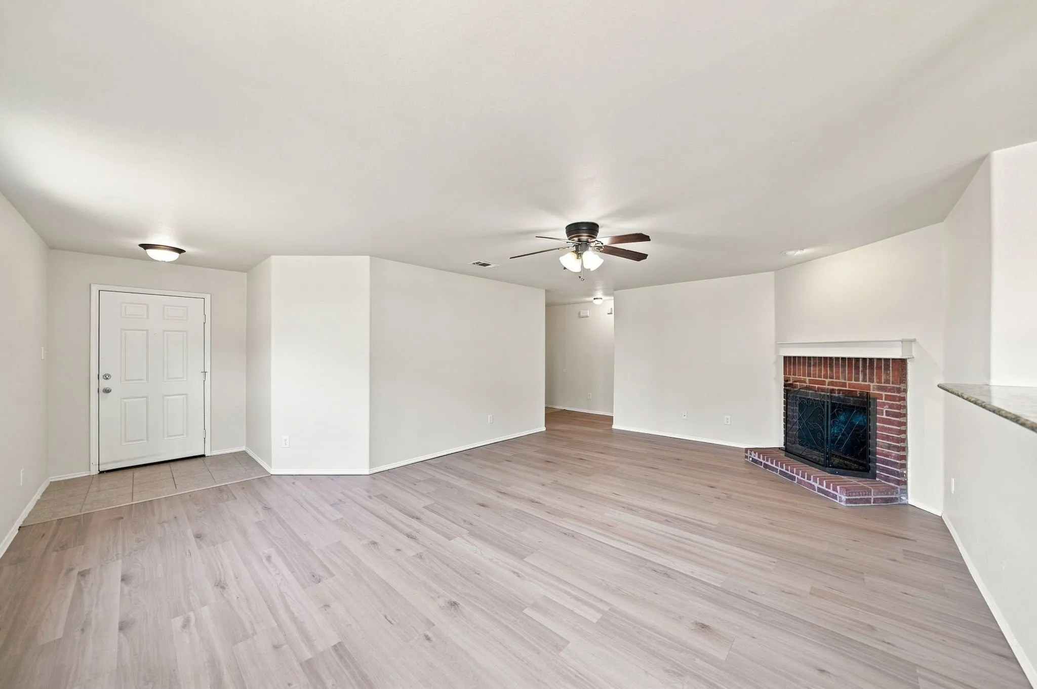 Spacious room with wood-finish flooring, a ceiling fan, and an exposed brick fireplace
