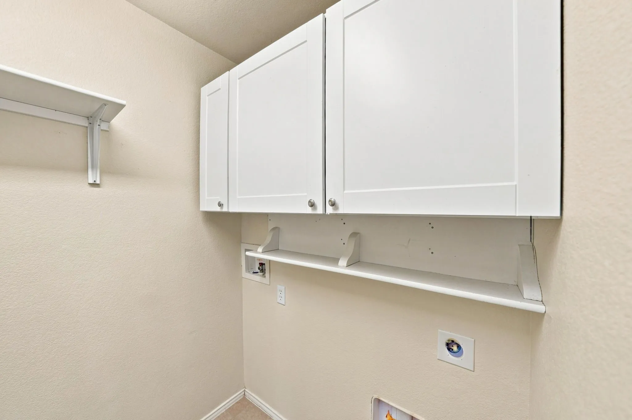 White shaker-style cabinetry, an integrated shelf with decorative brackets, a wall-mounted shelf, and light-toned wall finishes