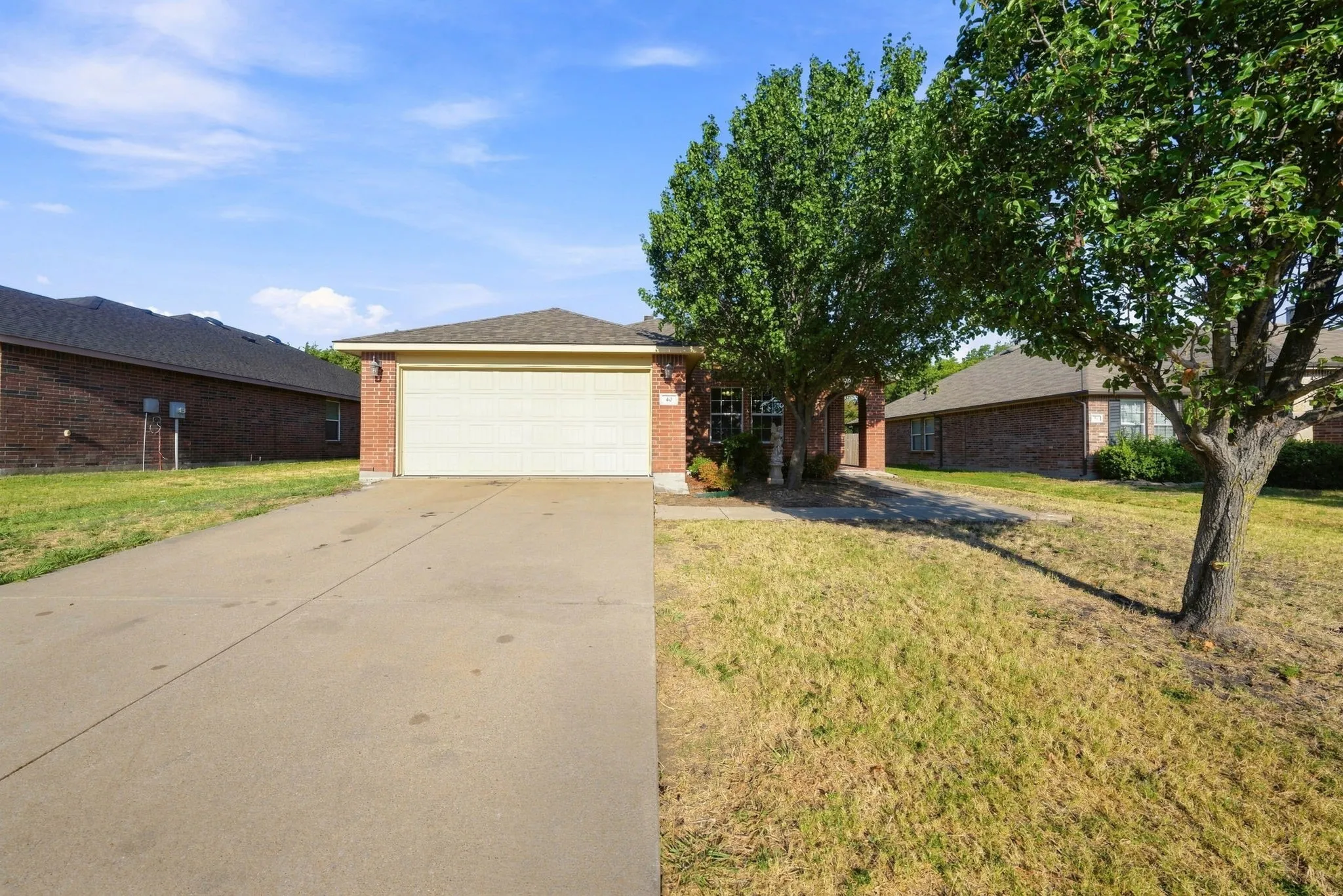 Brick exterior, attached garage, concrete driveway, mature trees