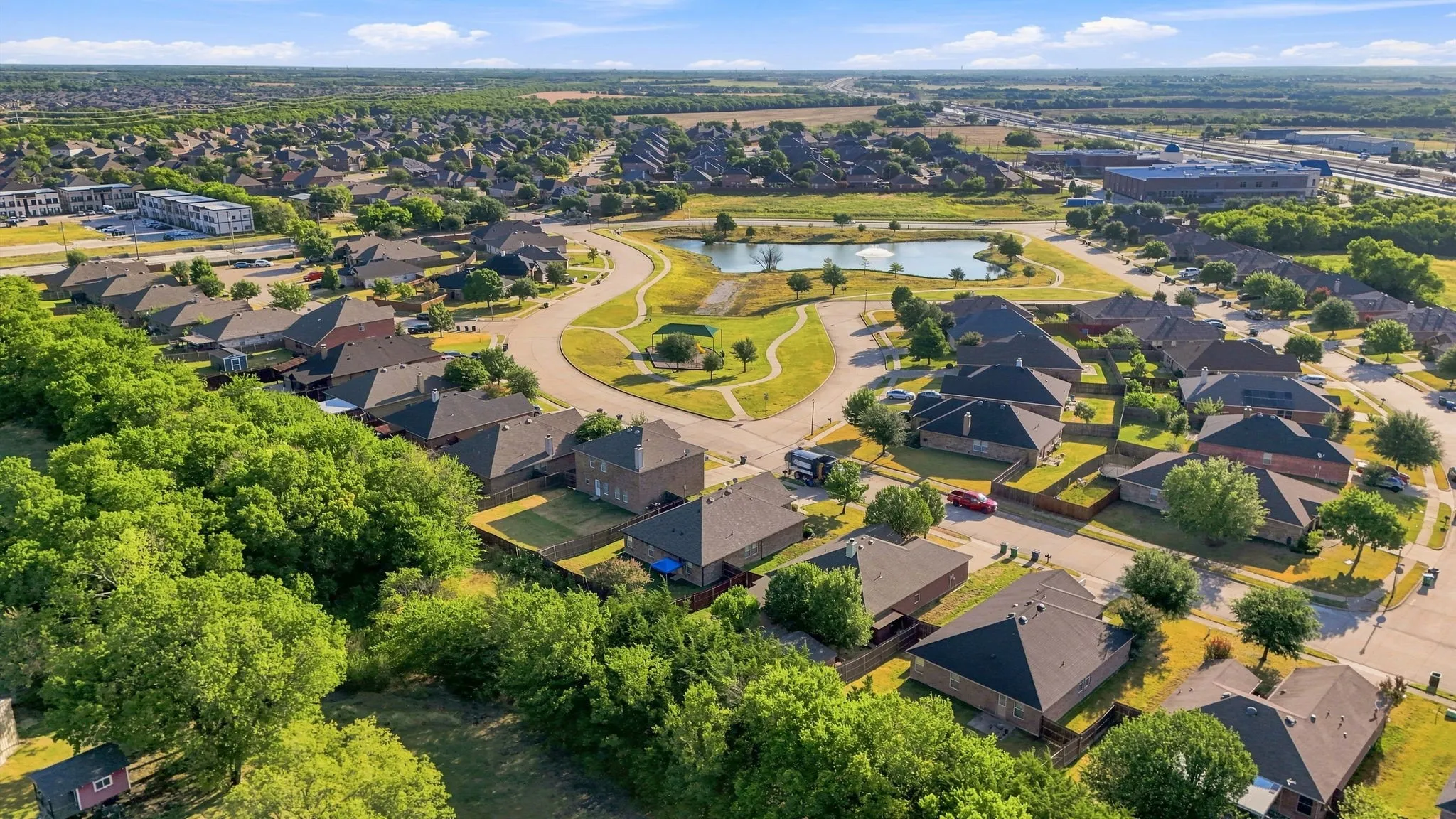 Expansive neighborhood featuring residential homes, a pond with a water feature, paved walking paths, and mature trees