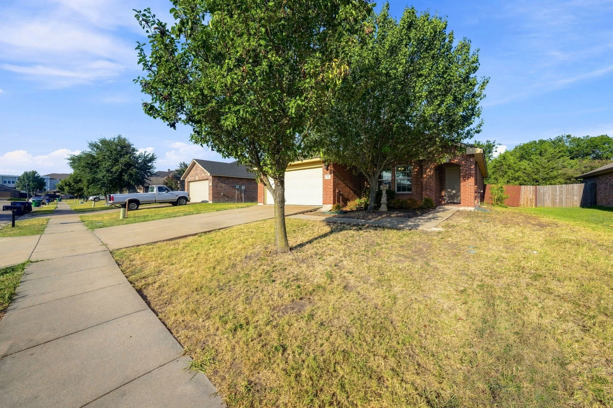Red brick exterior with an attached garage, concrete driveway, and mature front yard tree