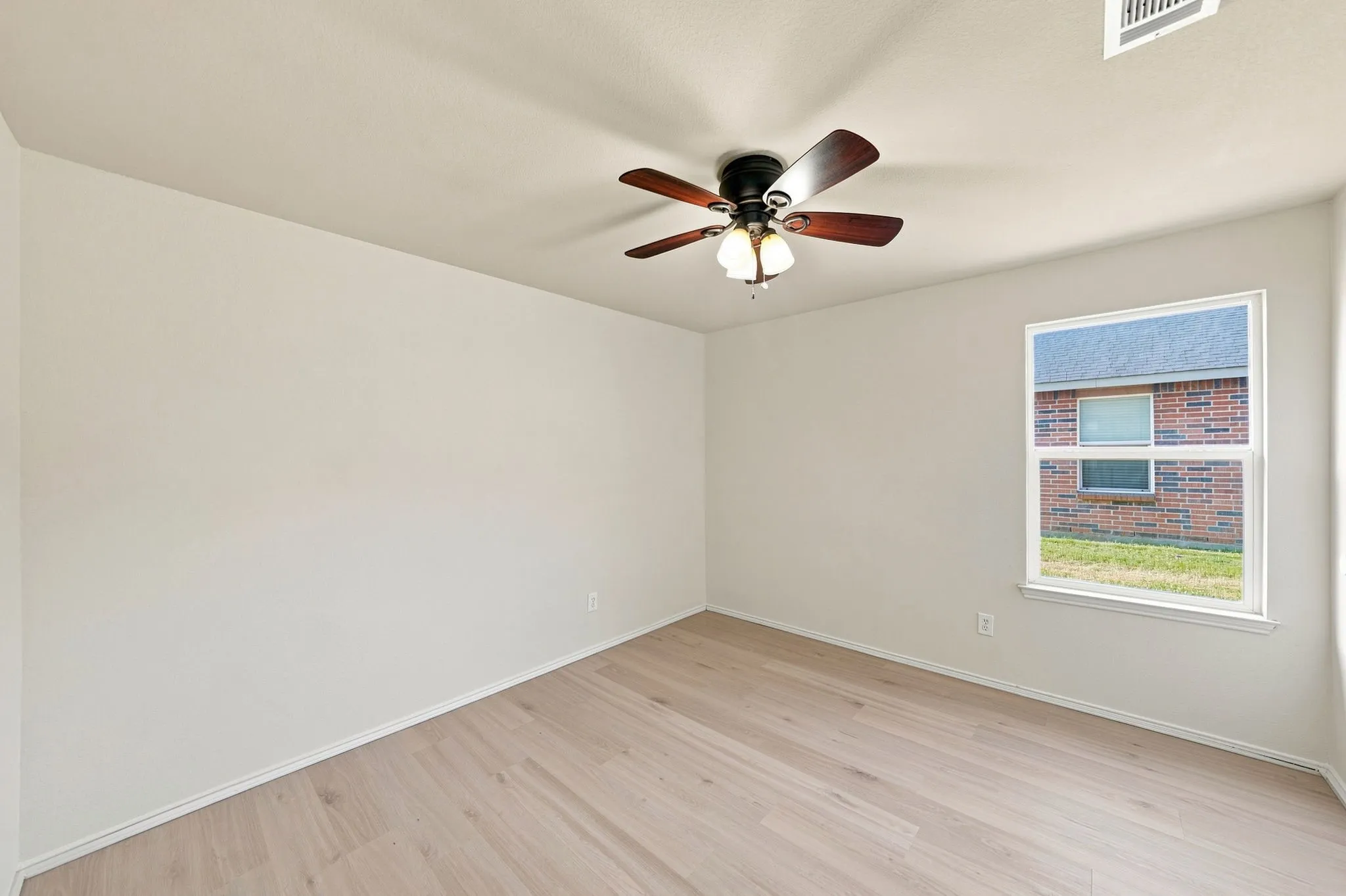 Wood-finish flooring, ceiling fan with integrated lighting, and a single window with white trim