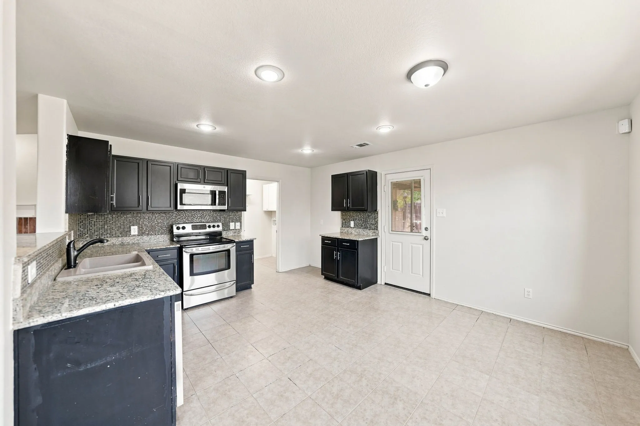 Kitchen featuring dark cabinetry, stainless steel appliances, granite-style countertops, mosaic tile backsplash, and tile flooring