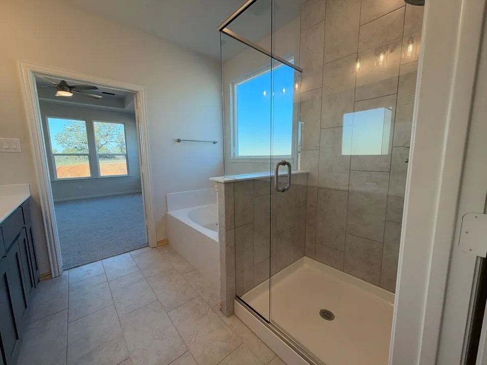 Spacious bathroom featuring a glass-enclosed shower with tile surround, a built-in soaking tub, and tile flooring