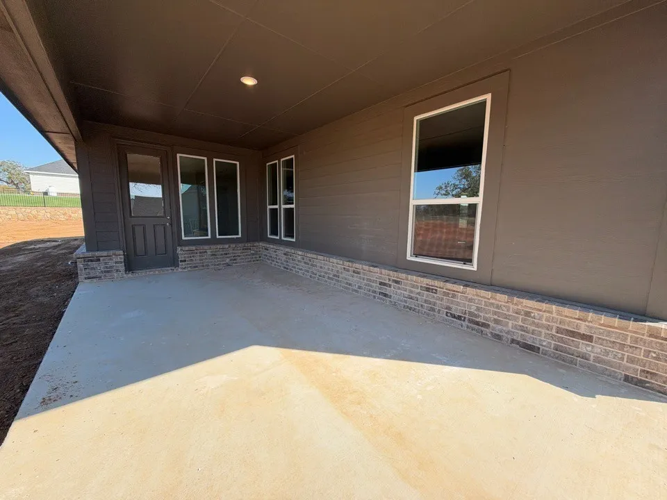 Covered concrete patio with recessed lighting, brick accent wall, and multiple windows