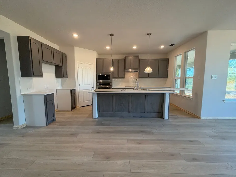 Modern kitchen featuring wood-finish flooring, recessed lighting, a kitchen island with pendant lighting, and dark-toned cabinetry