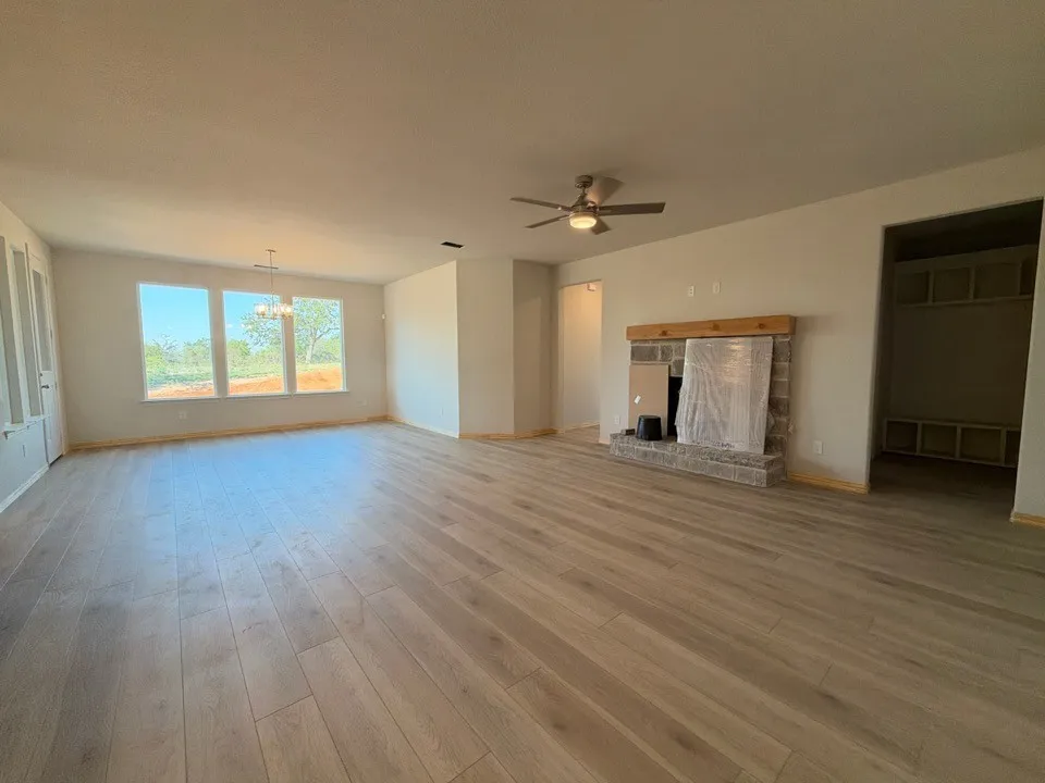 Expansive room featuring light wood-finish flooring, a stone fireplace with a wood mantel, a ceiling fan, and multiple windows