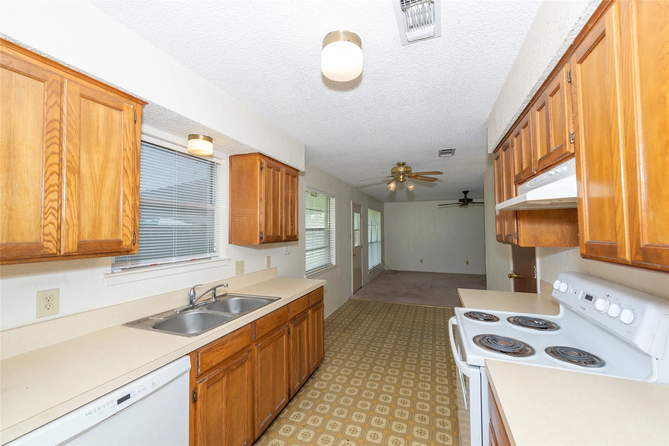 Galley kitchen featuring wood-finish cabinetry, laminate countertops, stainless steel sink with faucet, patterned tile flooring, and white electric range