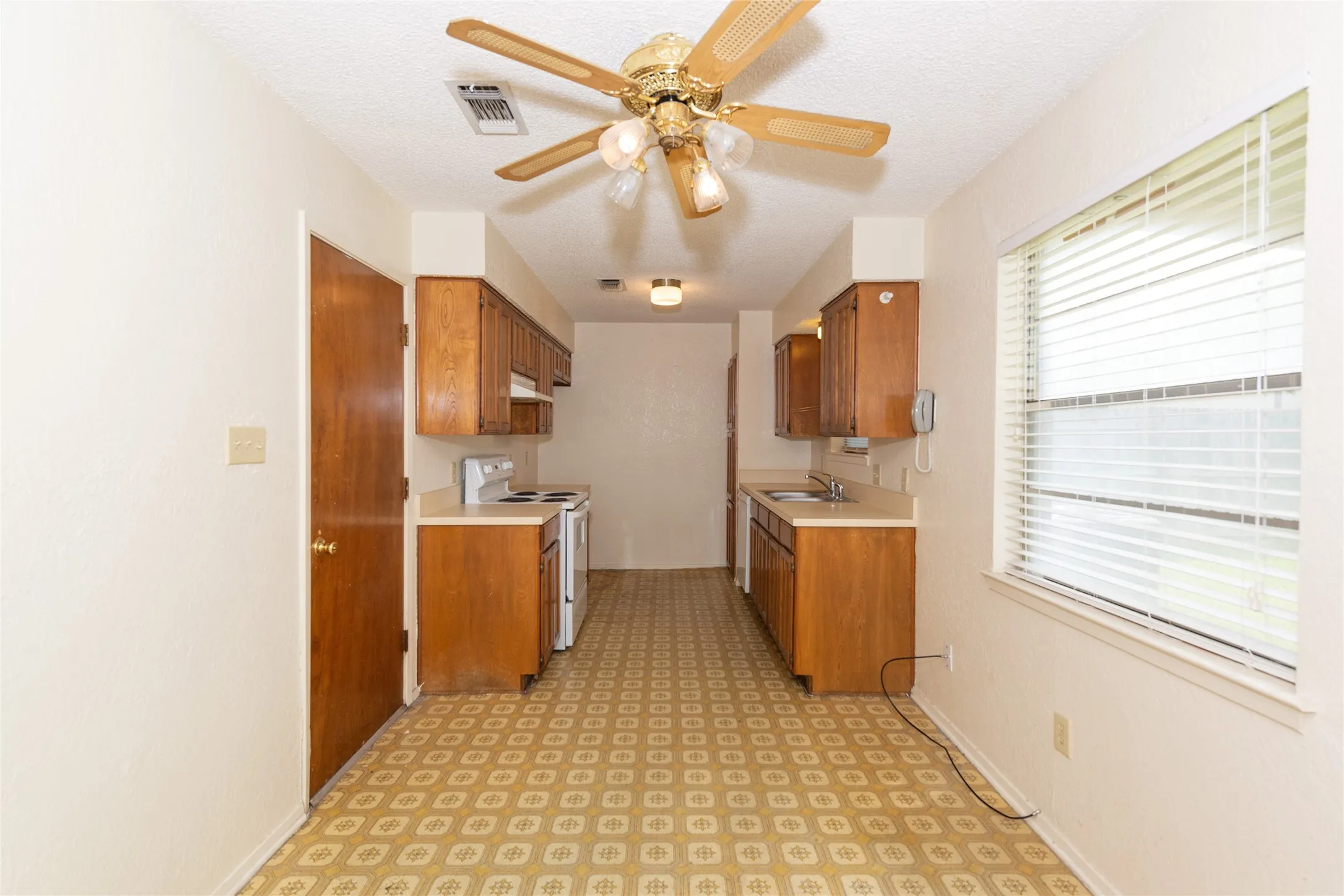 Galley kitchen with wood-finish cabinetry, light countertops, and ceiling fan