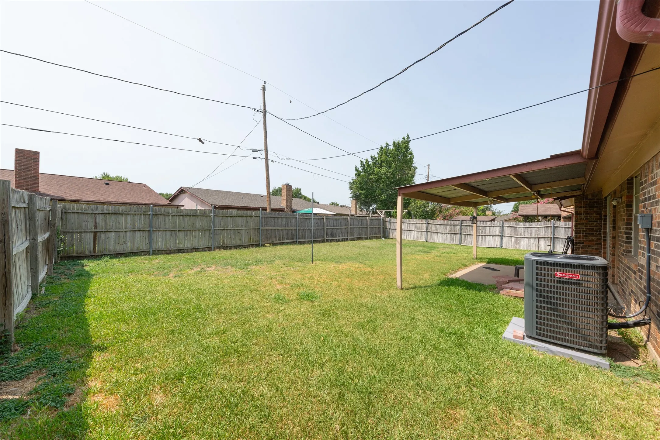 Expansive backyard featuring a manicured lawn, full wood fencing, and a covered patio area with a concrete slab