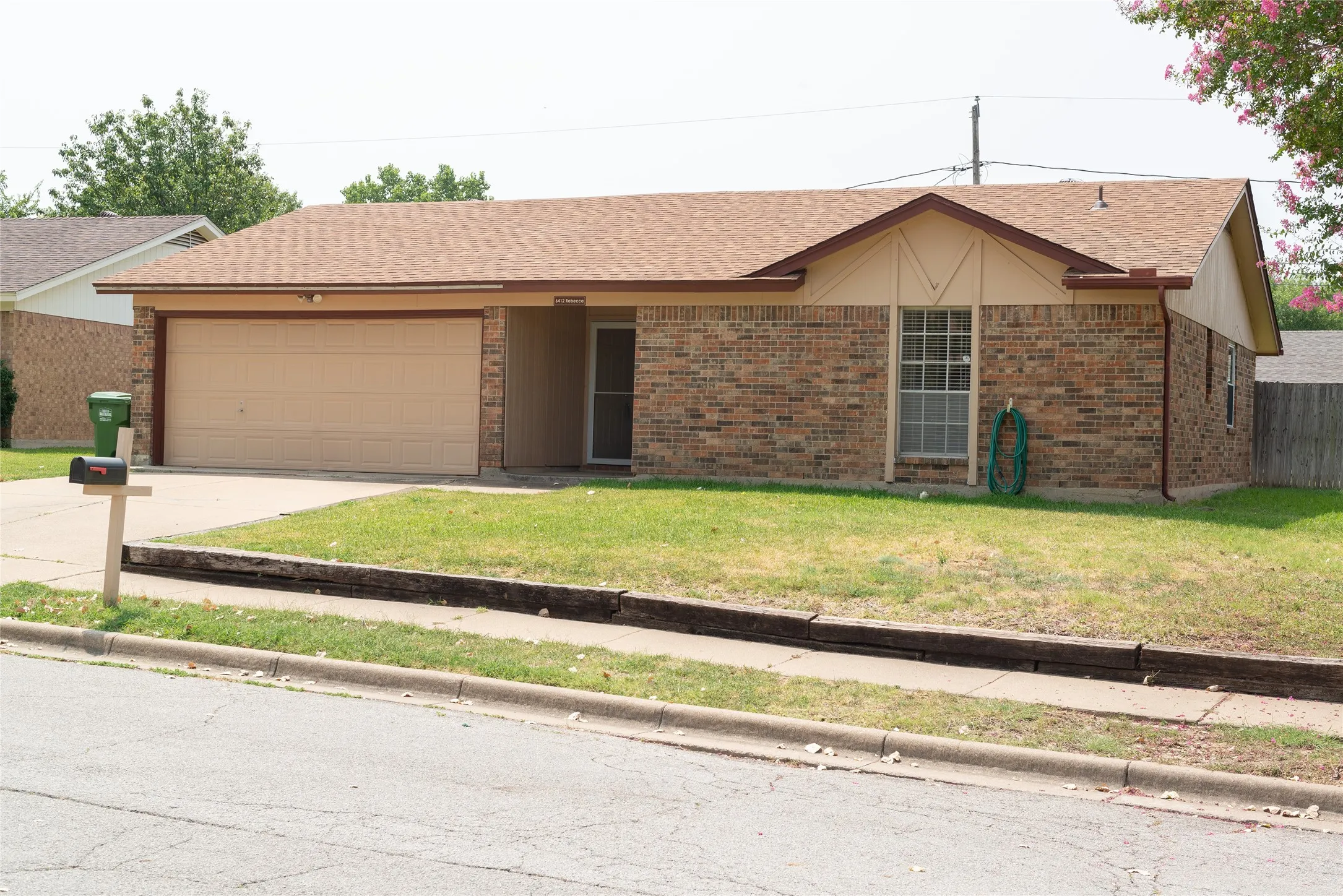 Brick exterior with a peaked roofline, attached garage, concrete driveway, and front lawn