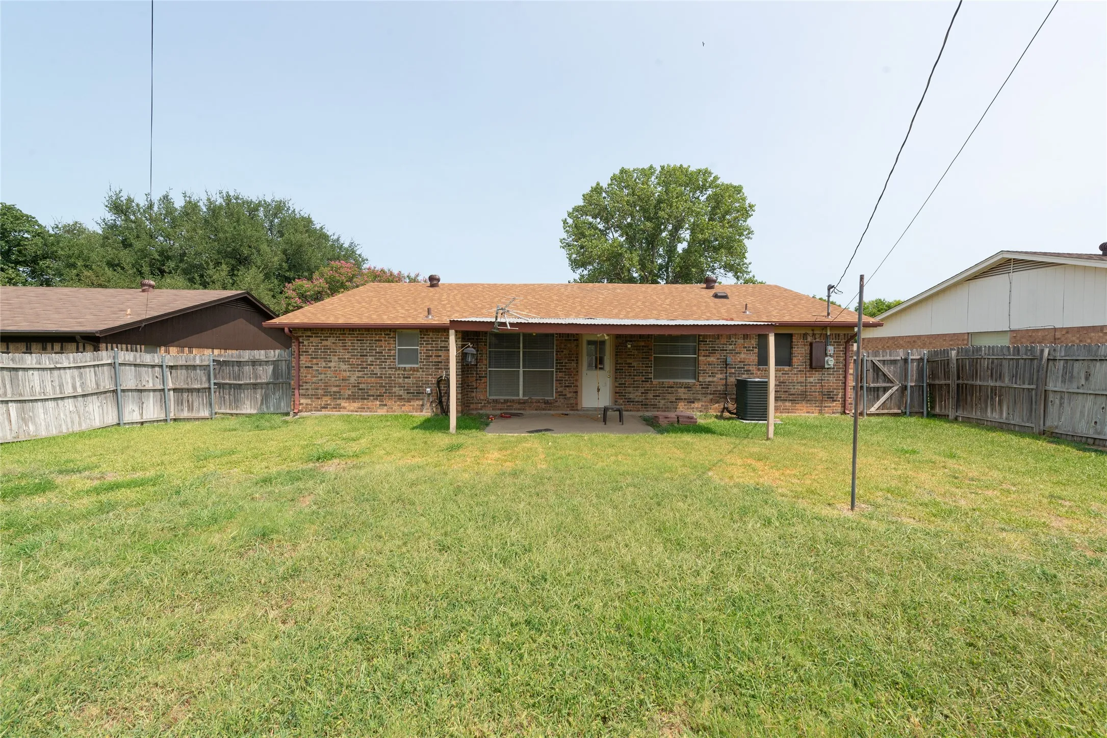 Expansive grass yard with wood fencing and a covered concrete patio
