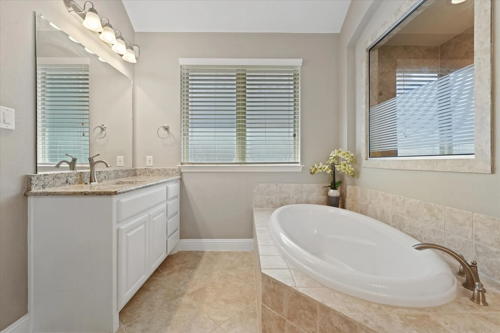 Relaxing soaking tub surrounded by tile, positioned beneath a large window with natural light and adjacent to the walk-in shower.