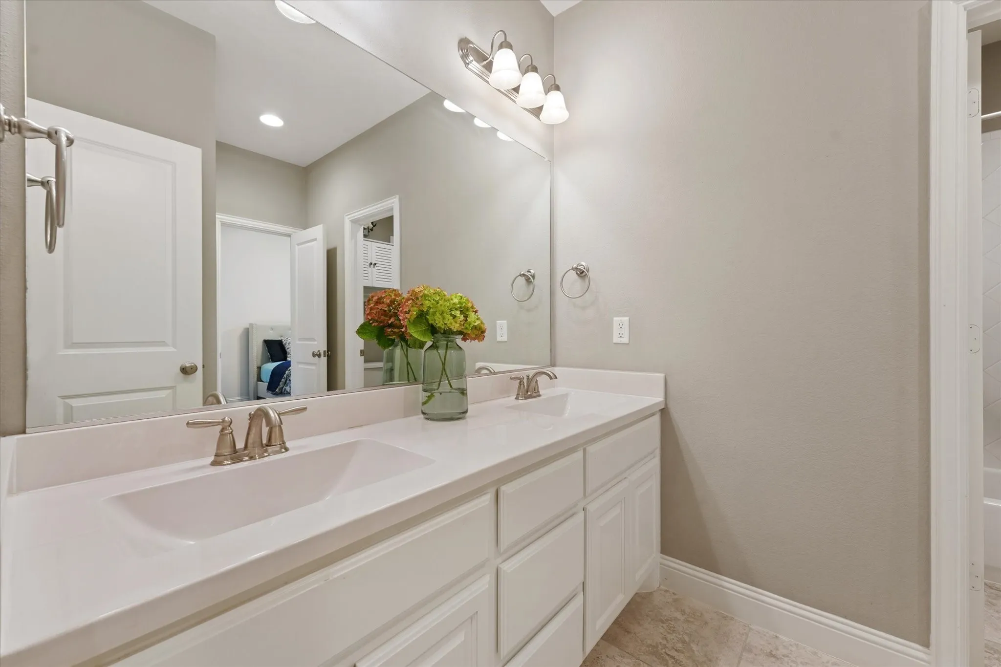 Full secondary bathroom with dual sinks, white cabinetry, large mirror and separate access to the tub and shower area.