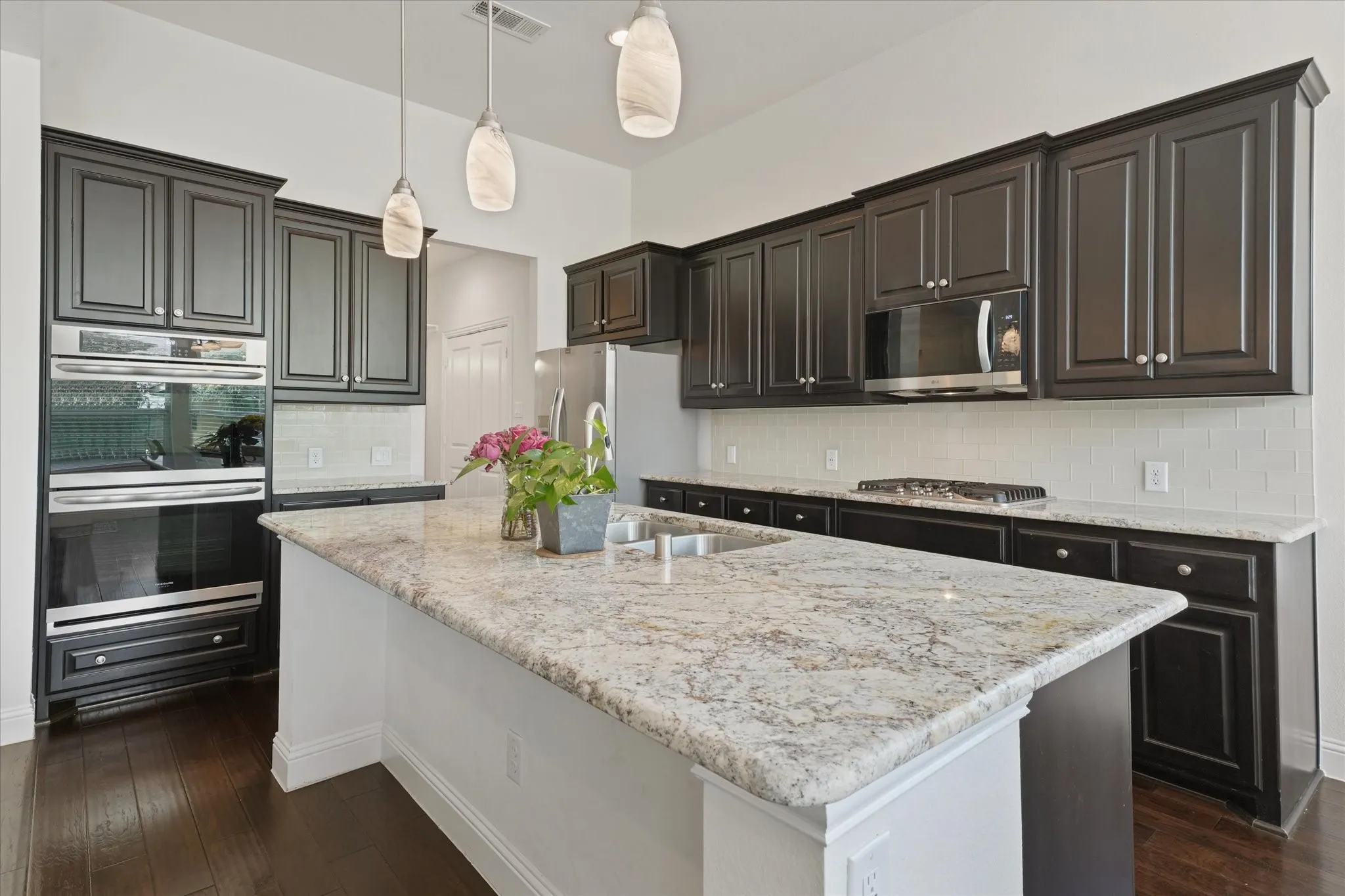 Large granite kitchen island with sink, dishwasher, seating space and open sightlines to the main living area.