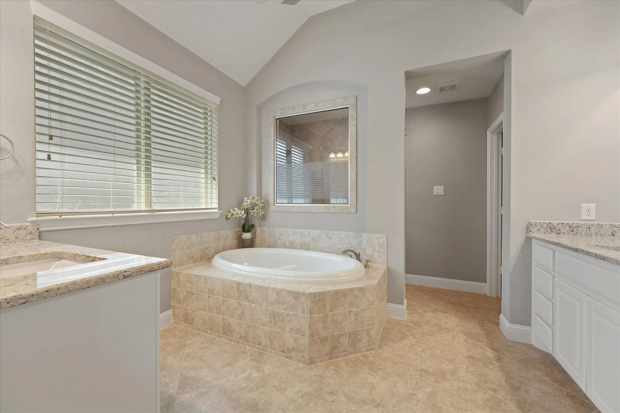 Primary bathroom with a soaking tub, granite countertops, separate vanities and direct access to the walk-in closet.