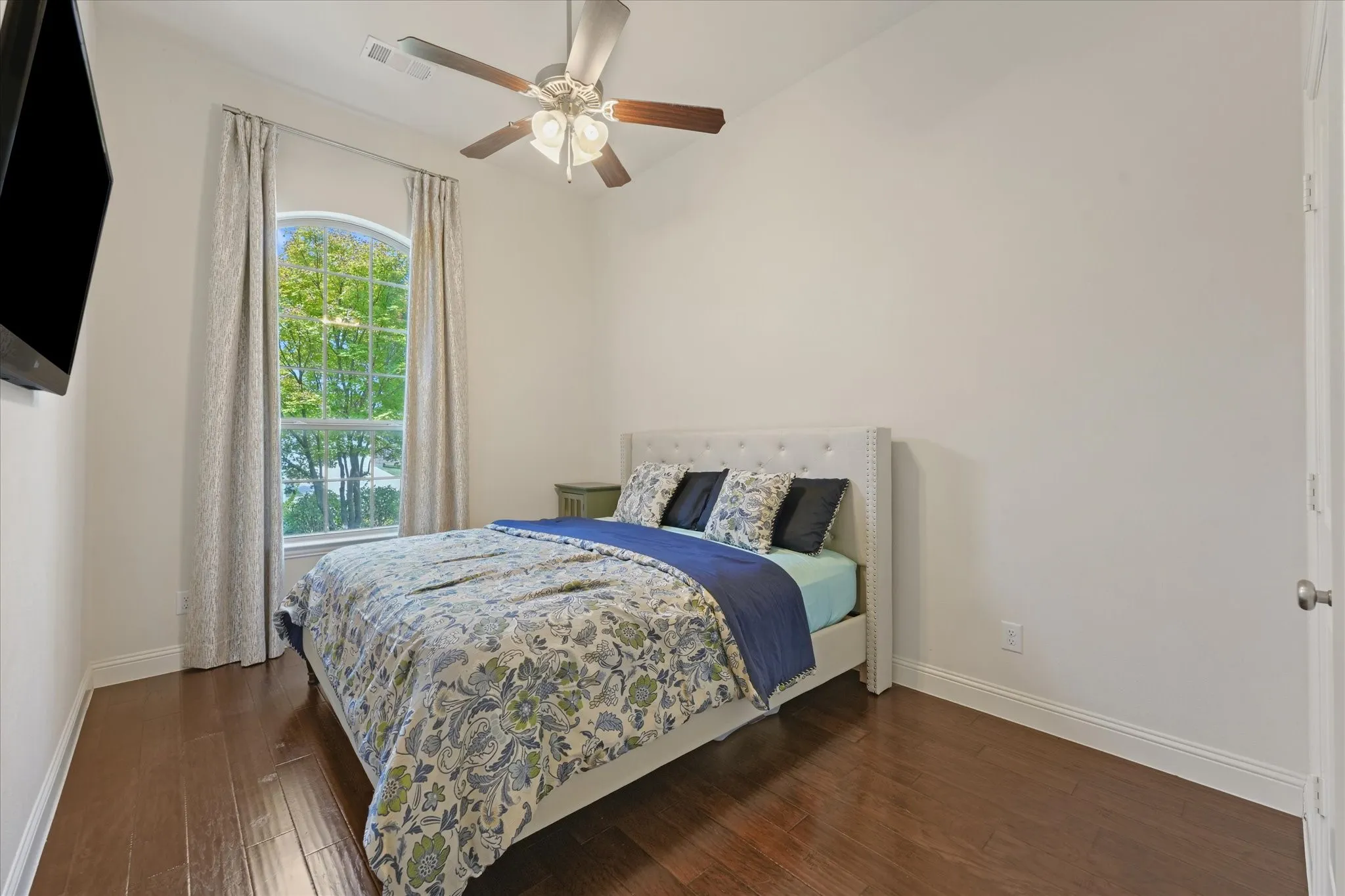 Third bedroom with hardwood flooring, vaulted ceiling, ceiling fan and a tall arched window overlooking the front yard.