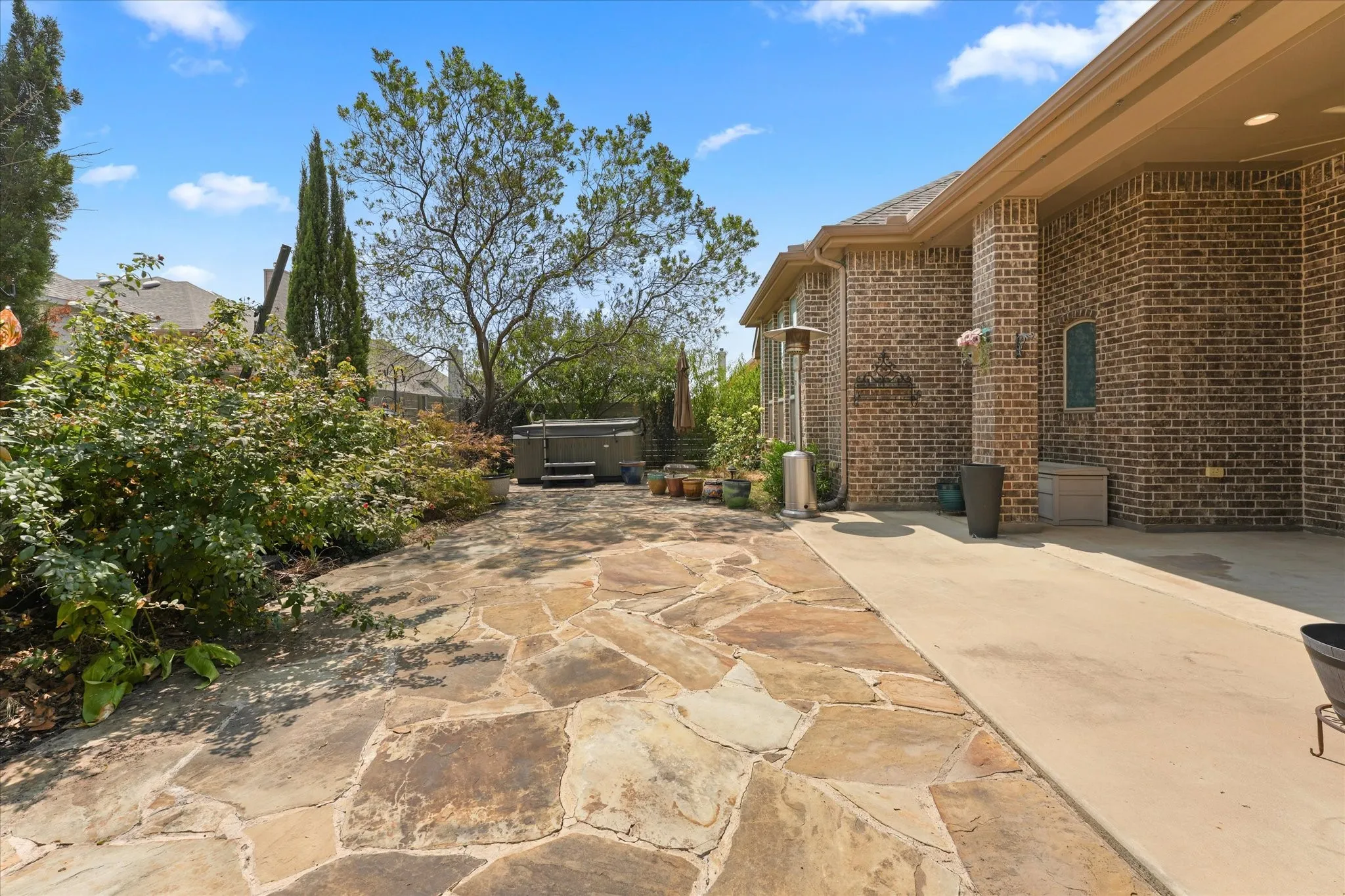 Private backyard featuring an extended flagstone patio, mature landscaping, hot tub and multiple areas for outdoor enjoyment.
