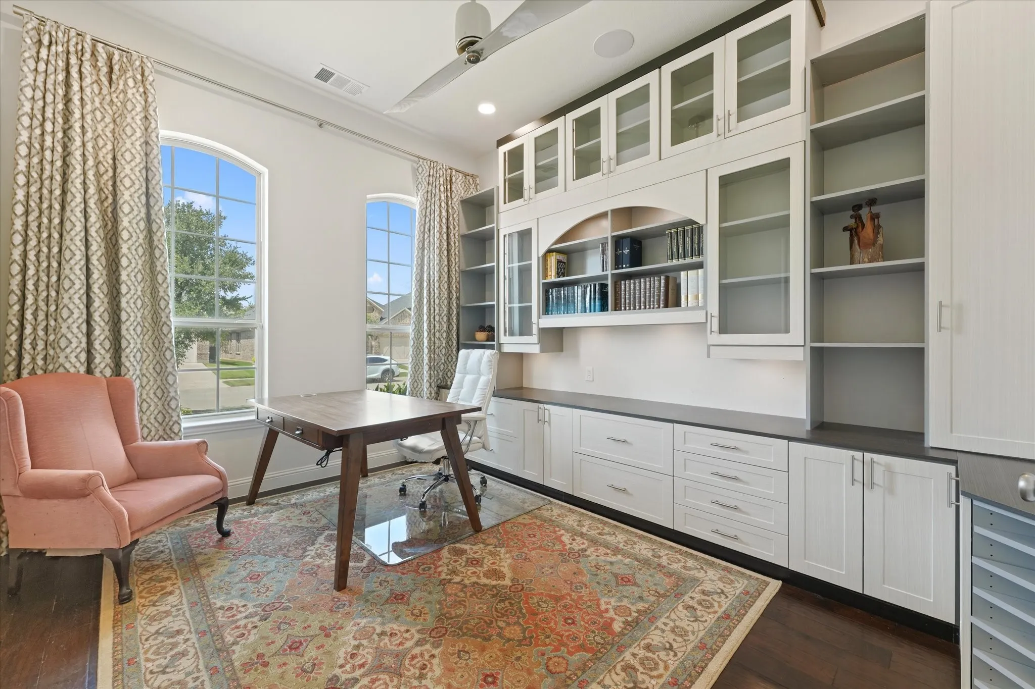 Private study with large windows, abundant natural light and extensive built-in cabinets, shelving and workspace for a home office.