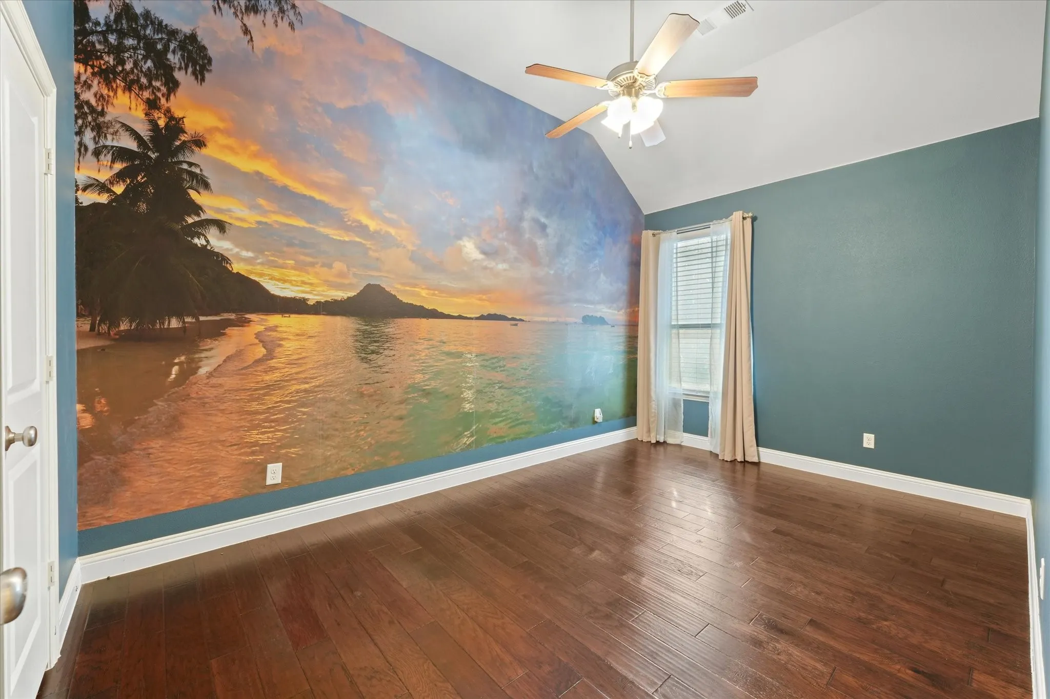 Secondary bedroom with vaulted ceiling, engineered hardwood flooring, ceiling fan and a large feature wall.