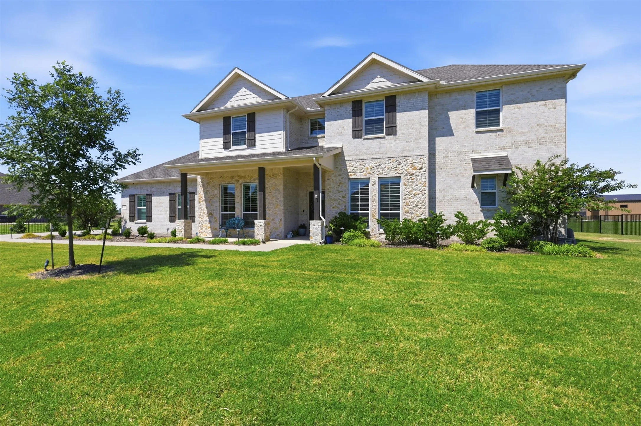 Two-story residence featuring a combination brick and stone facade, covered front porch, and mature landscaping