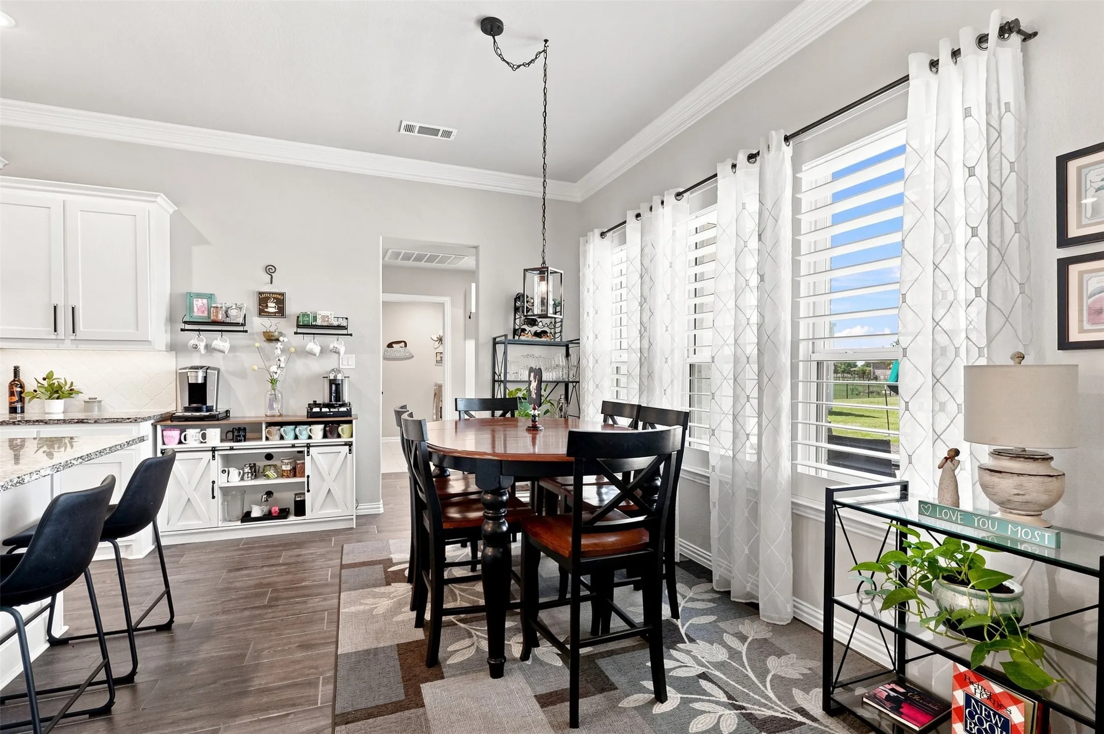 Spacious dining area featuring a dark wood-finish table with seating, multiple windows with plantation shutters, and crown molding