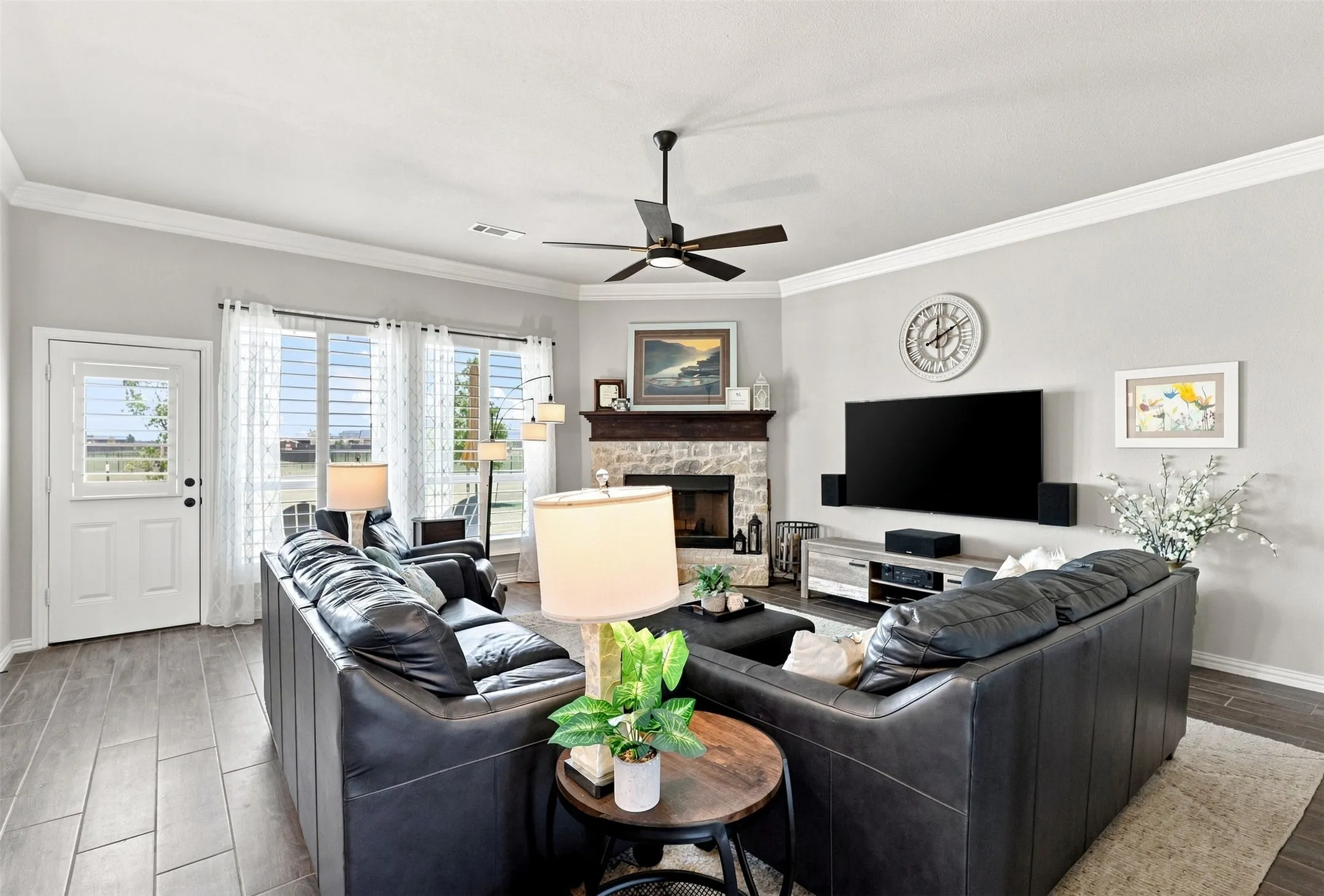 Living area featuring wood-finish flooring, a ceiling fan, a stone-surround fireplace with a wood mantle, and multiple windows
