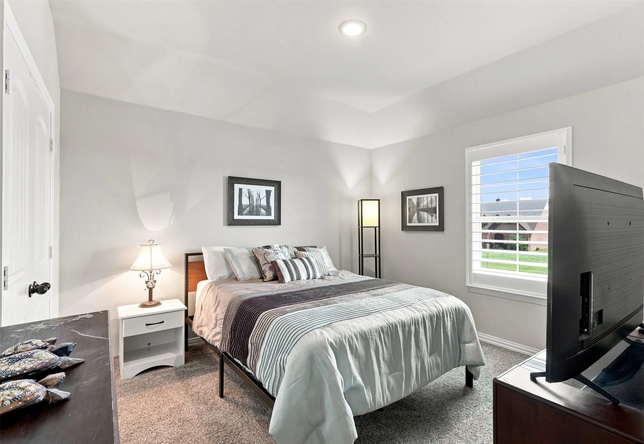 Bright secondary bedroom offering abundant natural light through large windows, dark wood-finish flooring, soft neutral wall tones, and coordinating bedding