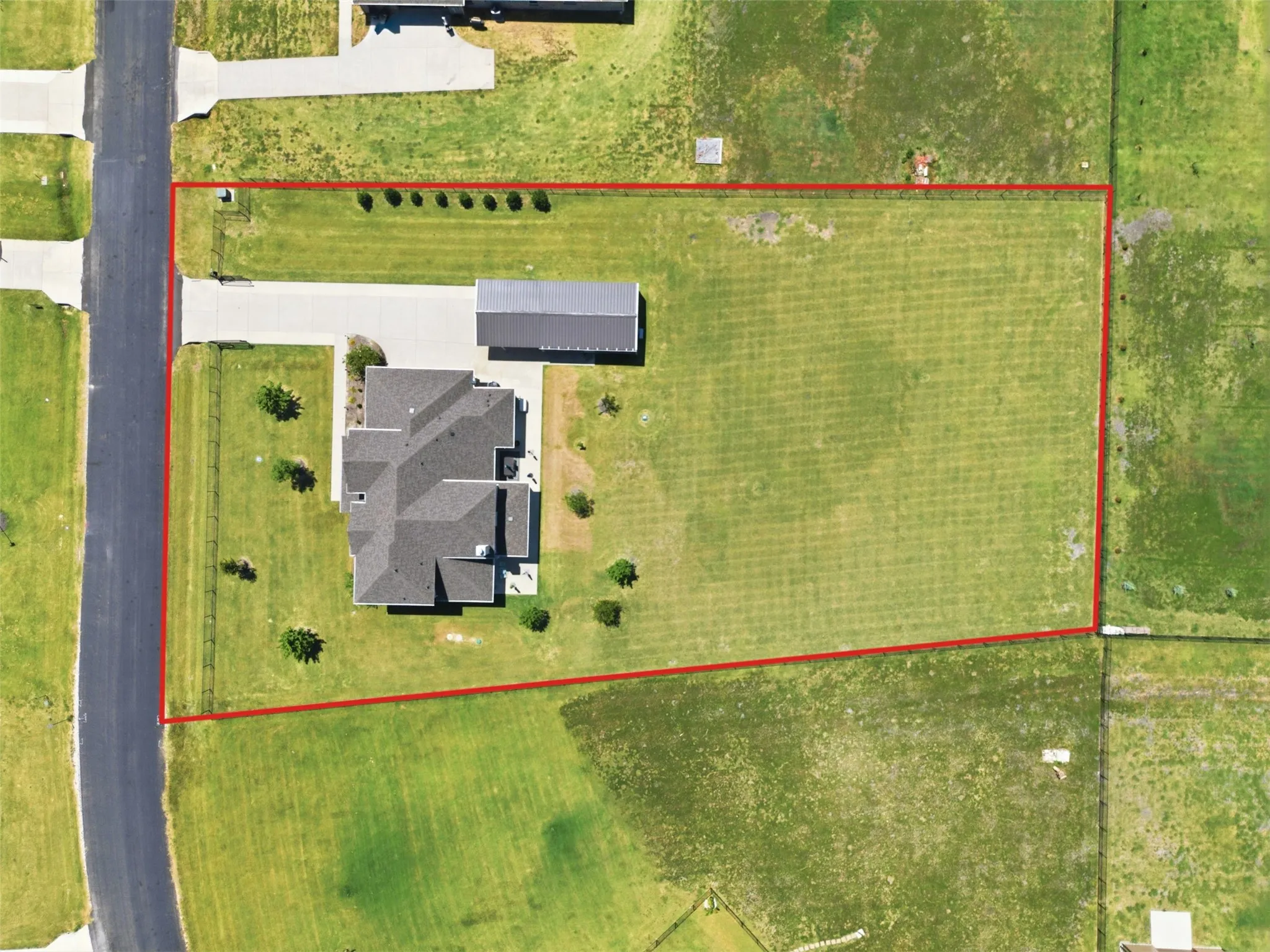 Expansive residential lot featuring a contemporary home with a dark-finished roof, surrounded by mature landscaping and established trees