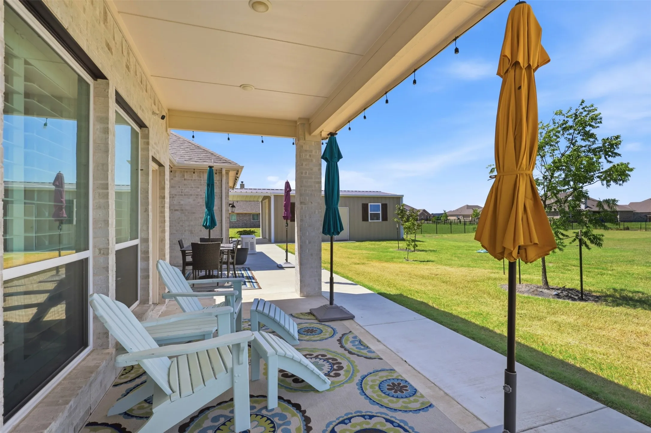Covered patio with concrete flooring and decorative area rug, featuring Adirondack seating, retractable umbrellas, and French doors providing direct access to the home
