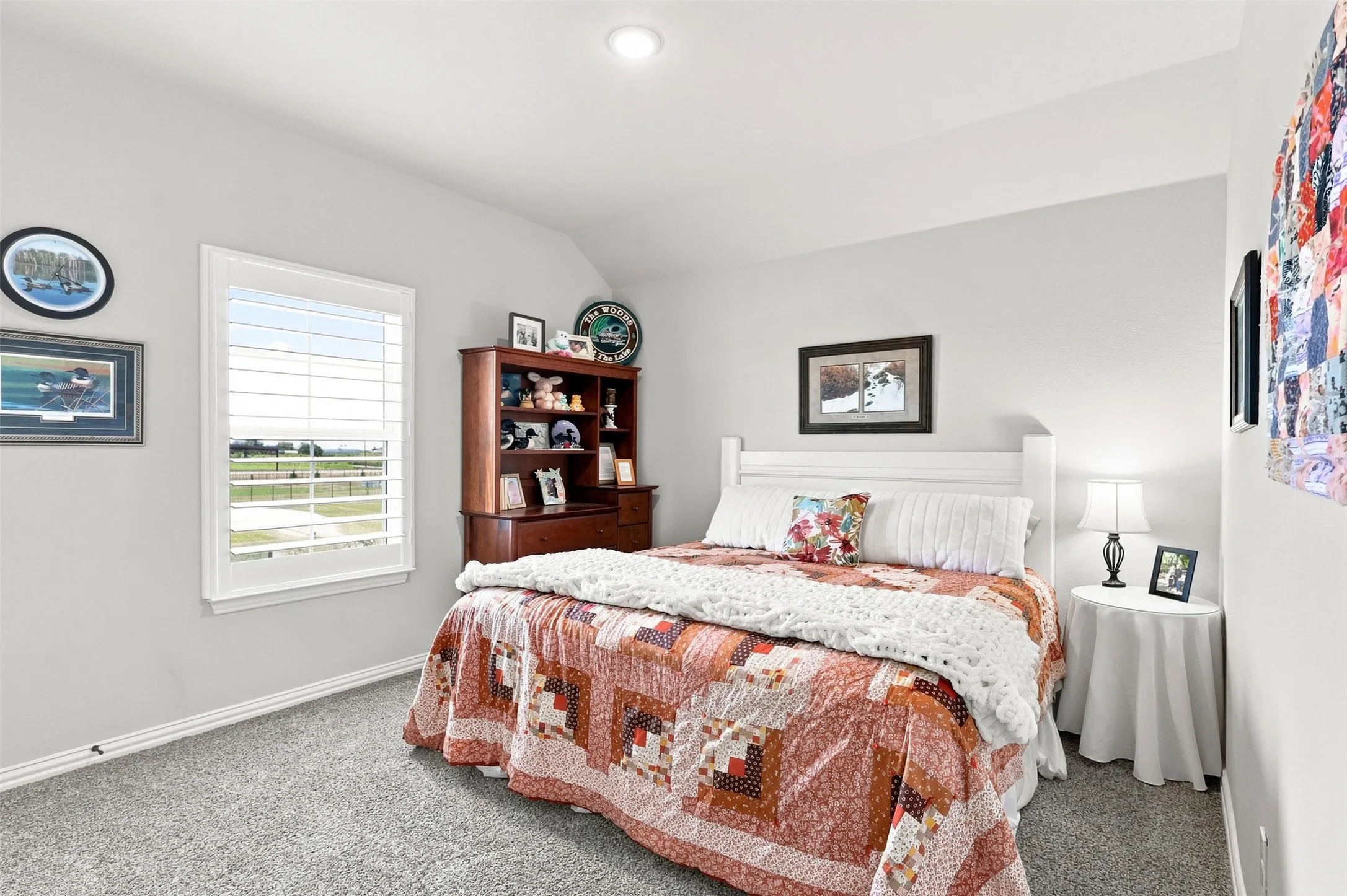 Bright secondary bedroom featuring neutral wall finishes, carpeted flooring, a white wooden bed frame, and large casement window with plantation shutters