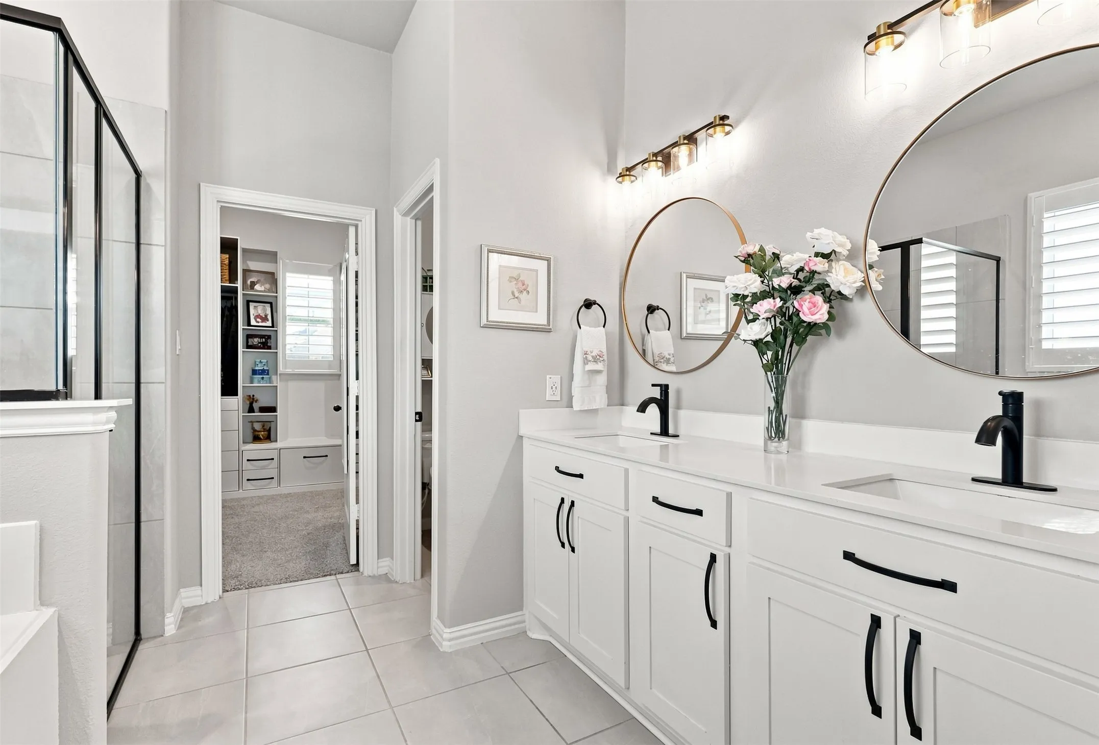 Spa-inspired primary bathroom featuring dual vanities with white cabinetry, black hardware accents, and integrated sink basins