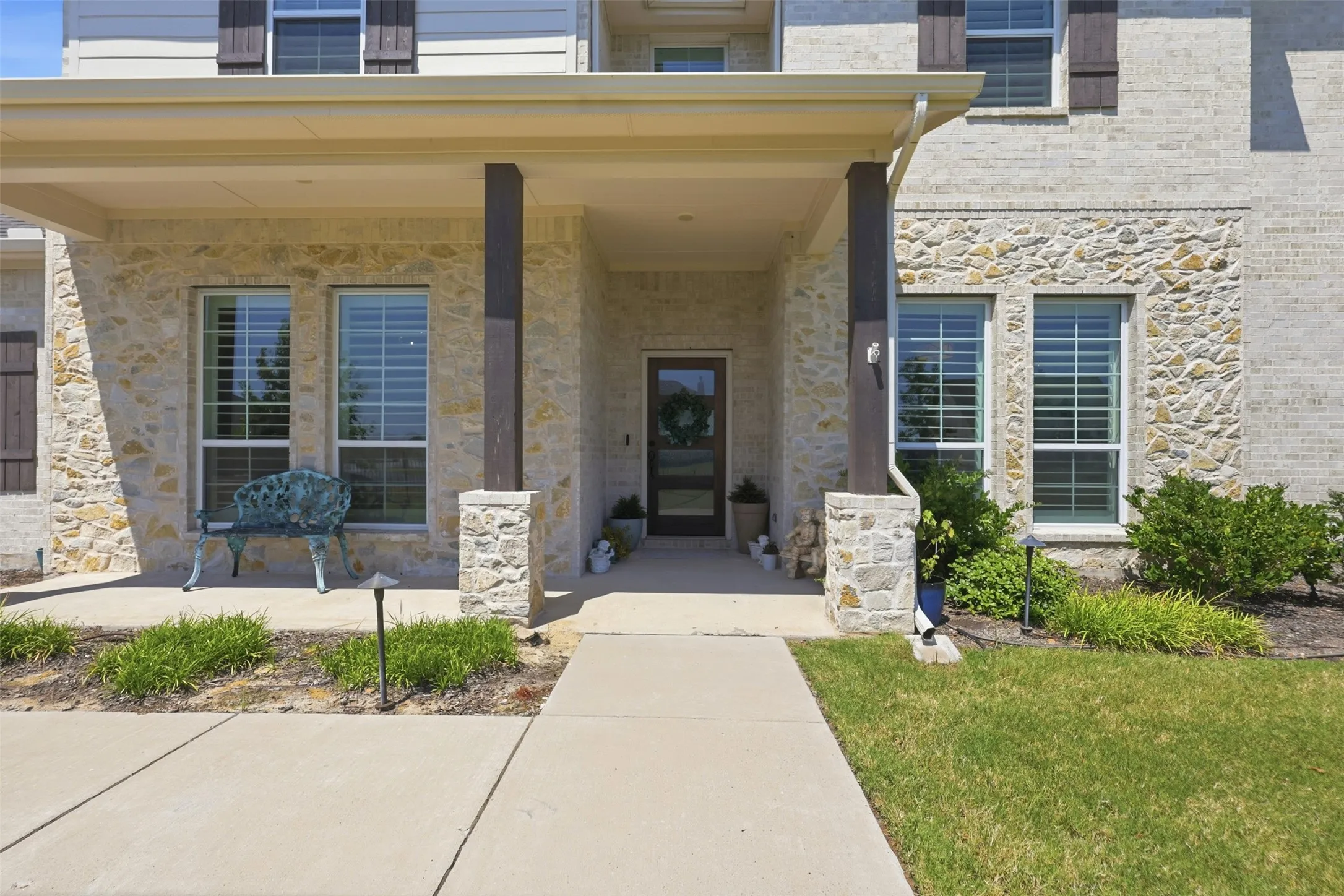 Stone facade with a covered entry, dark wood-finish support columns, and a concrete pathway