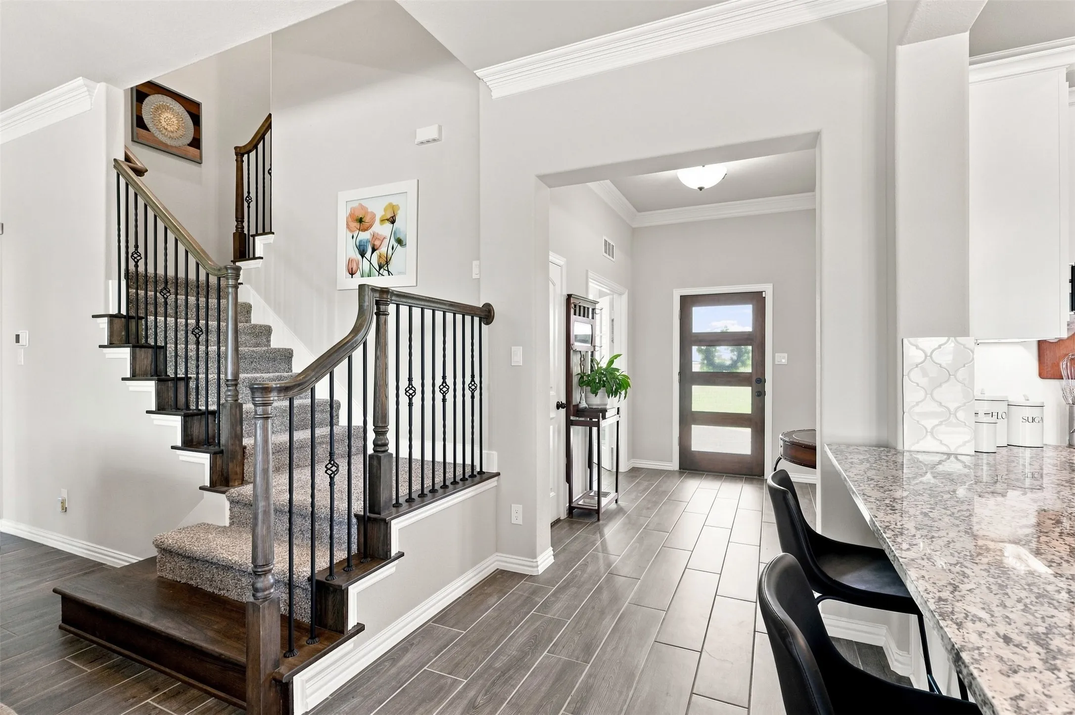 Staircase with wrought iron balusters and wood-finish handrails, complemented by wood-finish flooring extending into the entryway