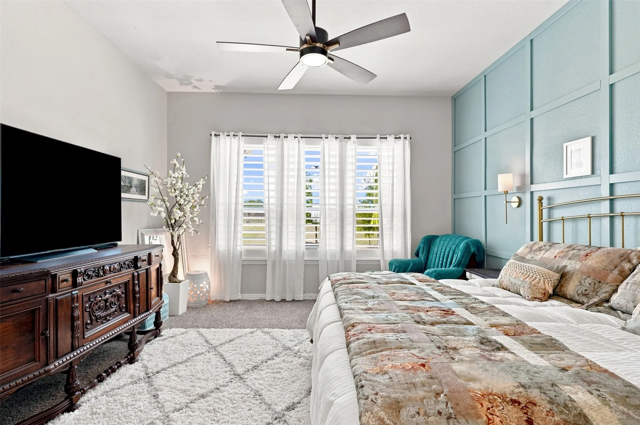 Primary bedroom suite featuring a tufted upholstered bed frame, layered bedding with patterned accents, and an accent wall with decorative paneling in soft blue-green tones