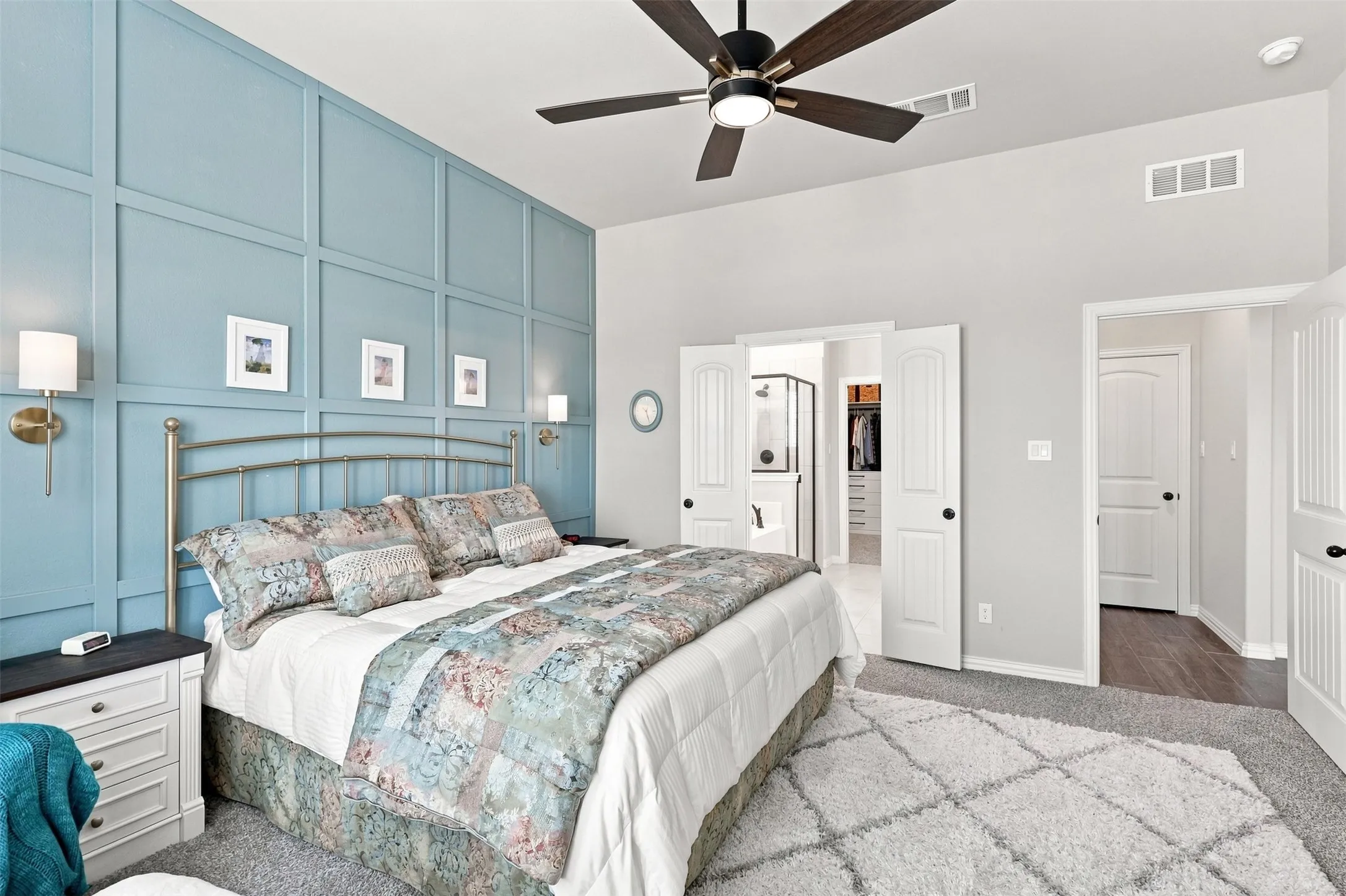 Primary Bedroom with Custom Wall Paneling, Ceiling Fan, and Hardwood FlooringThis spacious bedroom showcases floor-to-ceiling light blue wall paneling with an integrated metal bed frame, complemented by white trim and multiple white doors providing access throughout